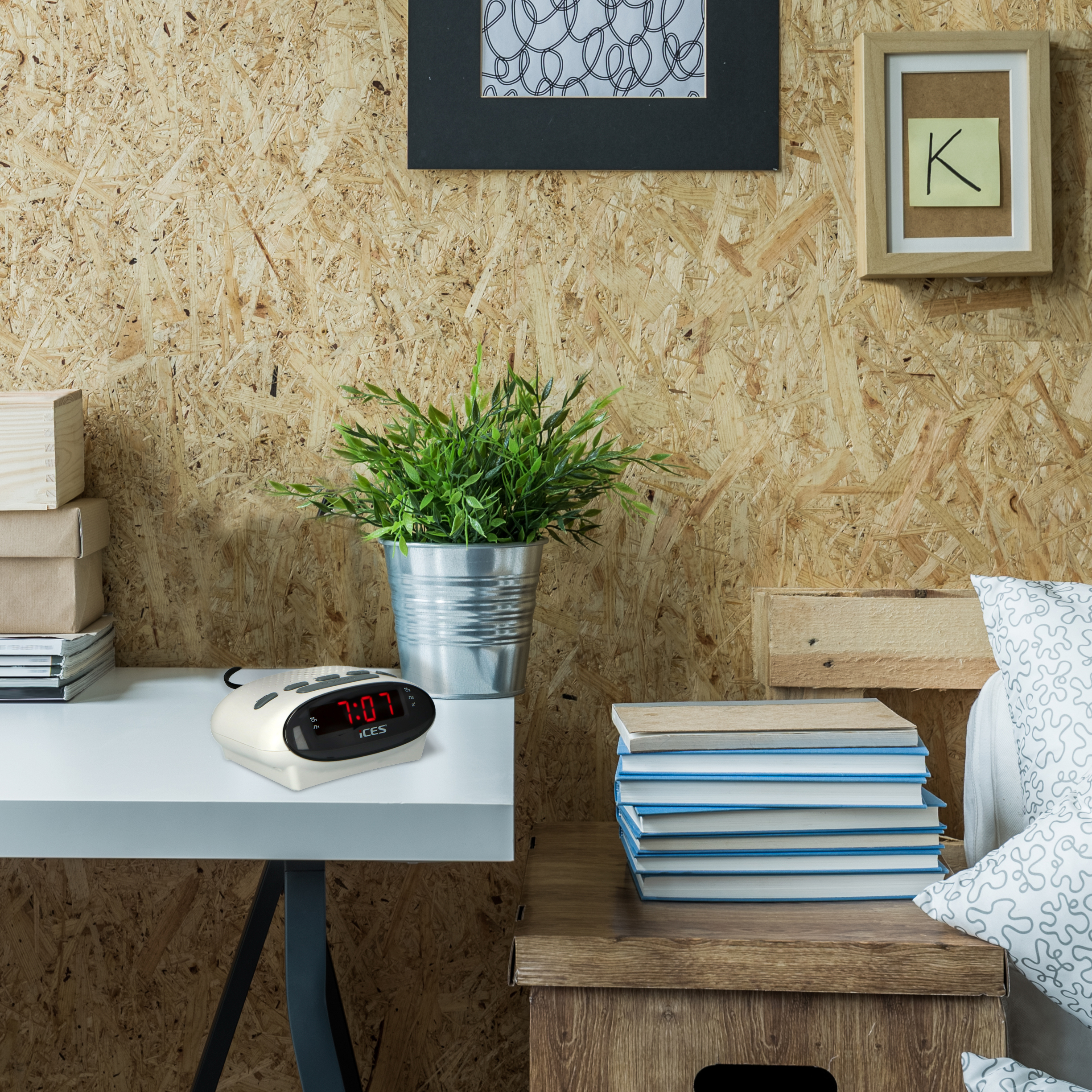 Biały zegar cyfrowy na białym stole. Książki i roślina po prawej. Drewniane tło.