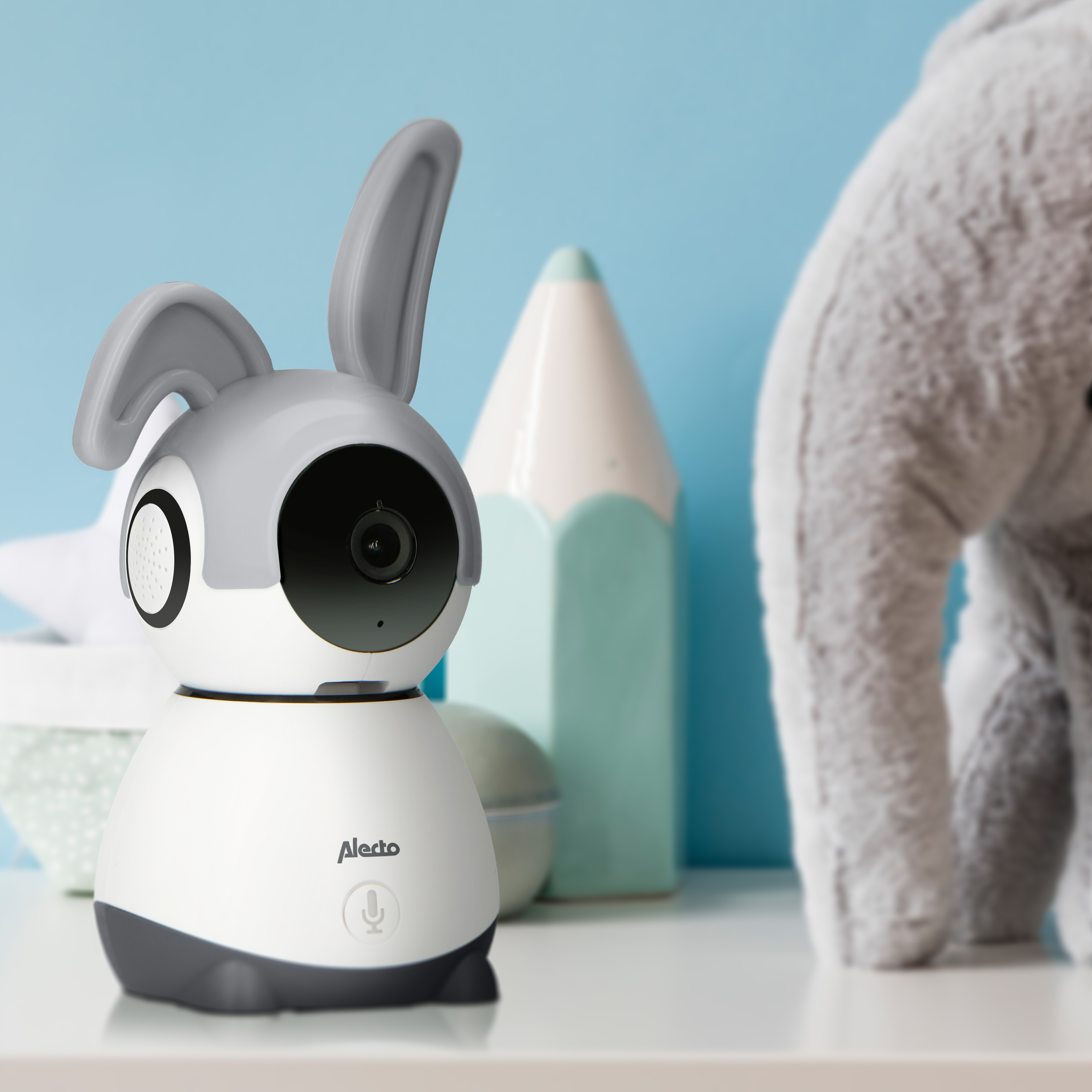 Ein weiß-grauer Babyphone in Hasenform. Blauer Hintergrund. Ein Bleistift und ein Stofftier.