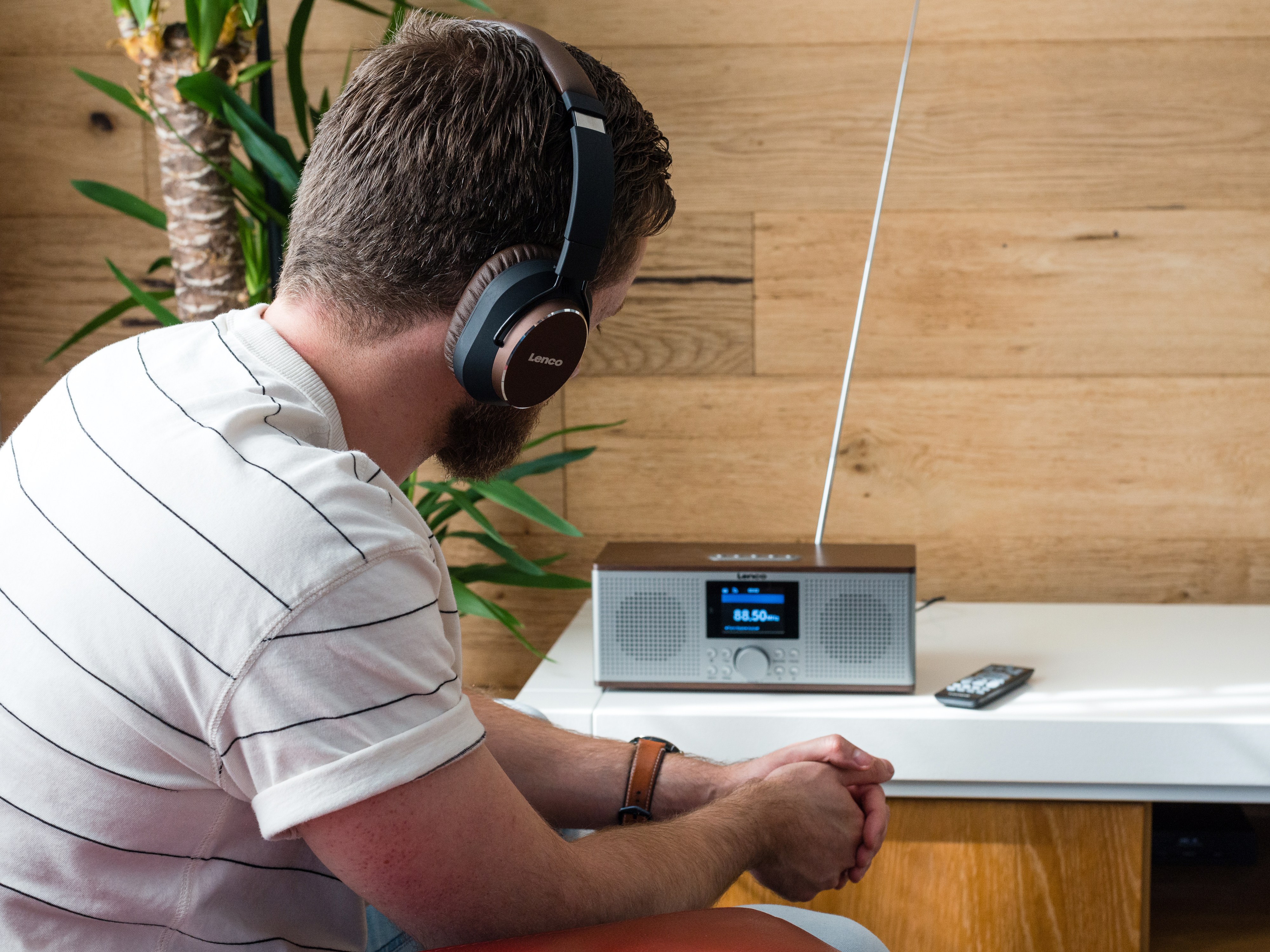 Mężczyzna w słuchawkach słucha radia na tle drewnianej ściany.
