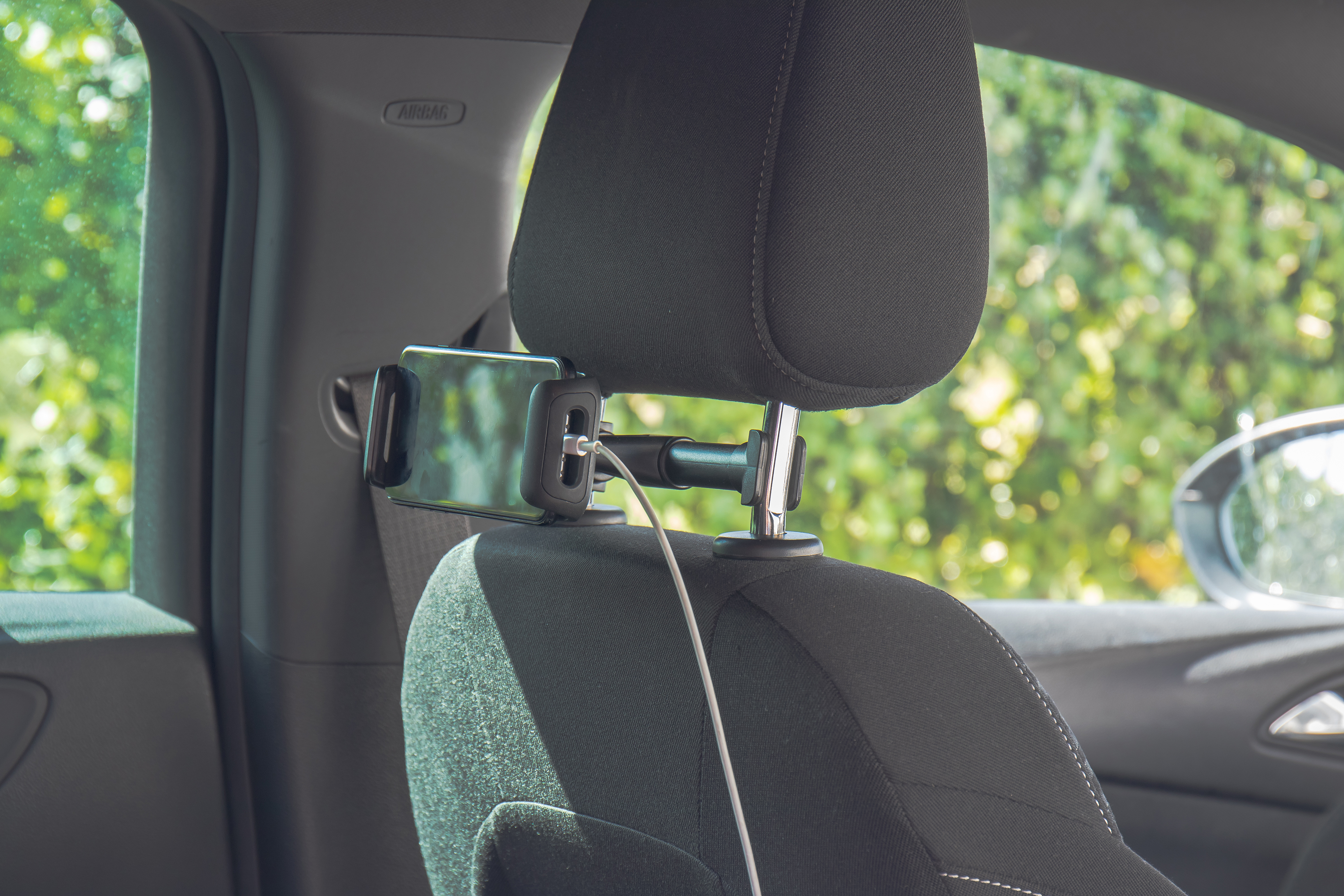 Eine Kopfstütze im Auto mit einem daran befestigten Telefon, Ladekabel eingesteckt, im Auto.