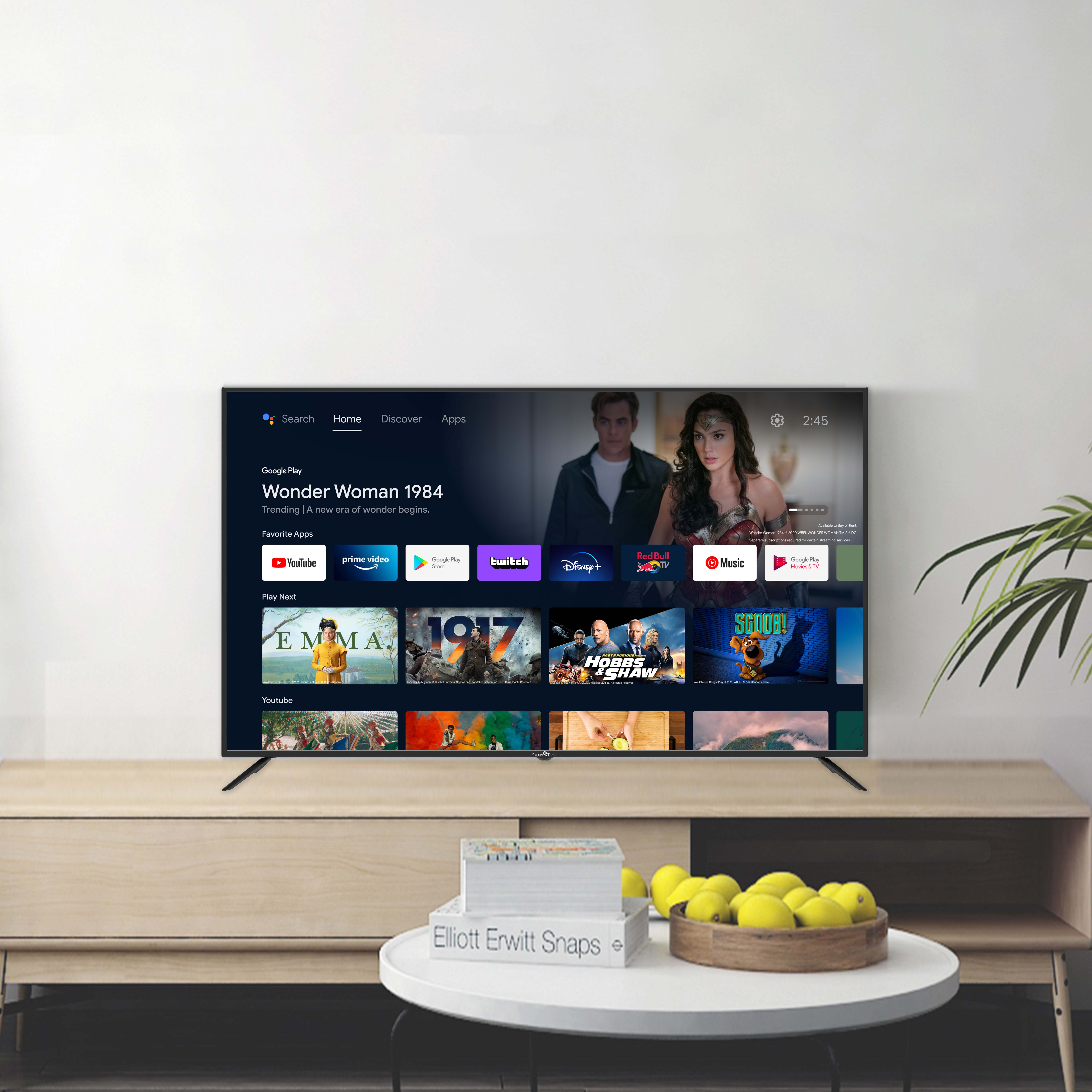 Una gran pantalla de TV que muestra una película, con un mueble de madera debajo. Las paredes son blancas.