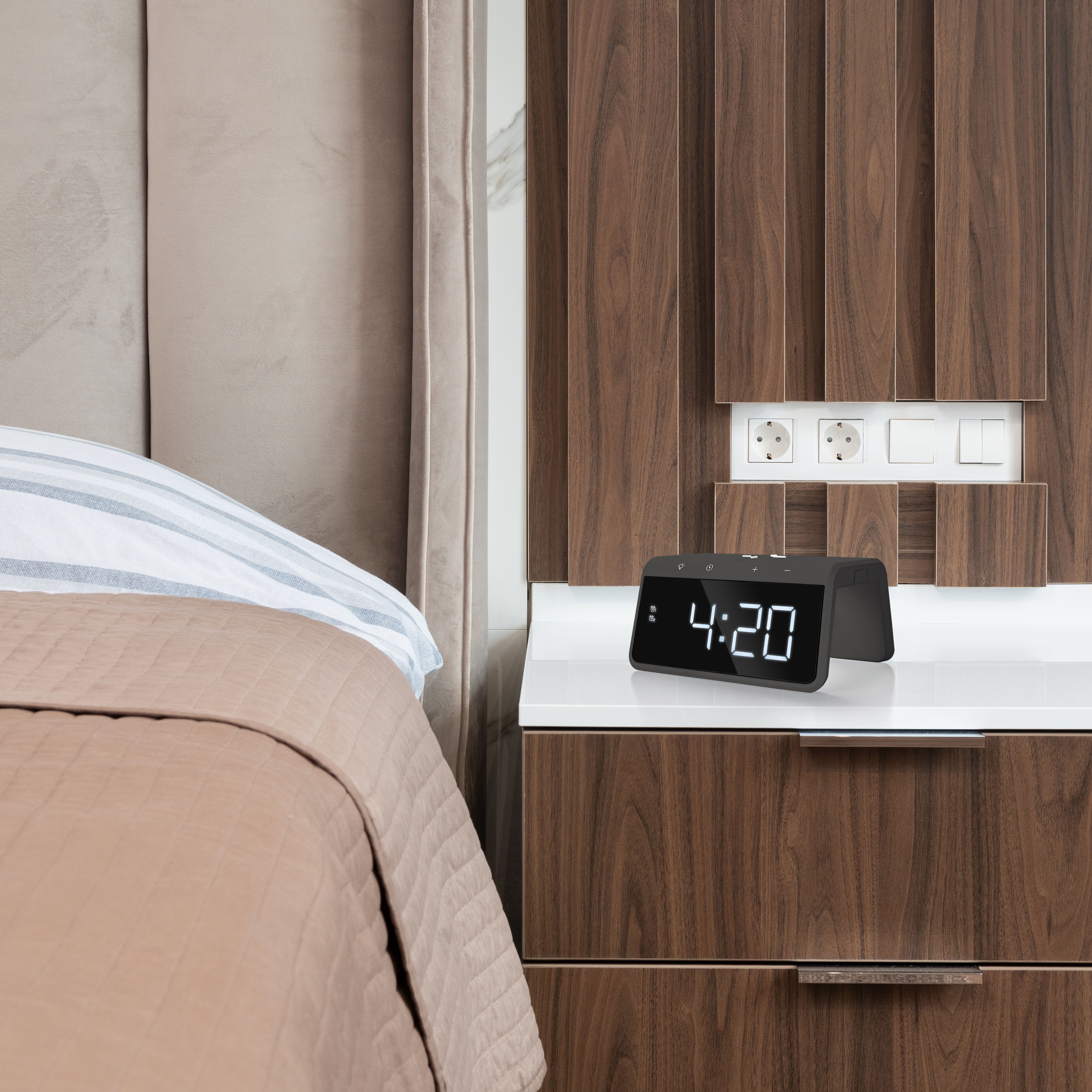 Black digital clock displaying 4:20 on a white nightstand.  Bed and wooden wall in the background.