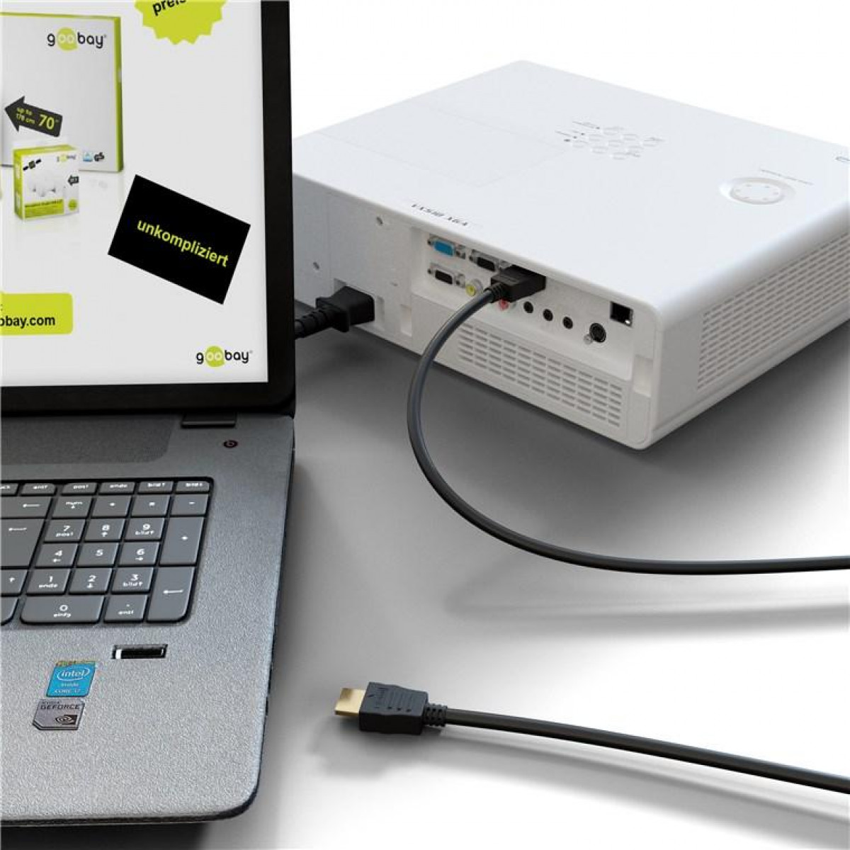 Ein Laptop, der mit einem weißen Projektor mit schwarzem Kabel verbunden ist, auf grauer Oberfläche.