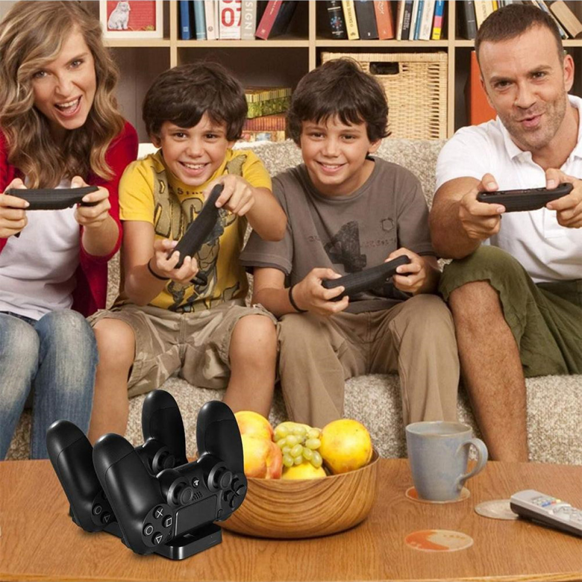 Quattro persone che giocano ai videogiochi su un divano. C'è una ciotola di frutta e una tazza su un tavolo.