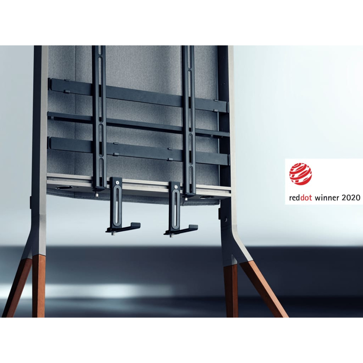 Un moderno supporto TV con tessuto grigio e gambe in legno. Un logo Red Dot Winner 2020 a destra.