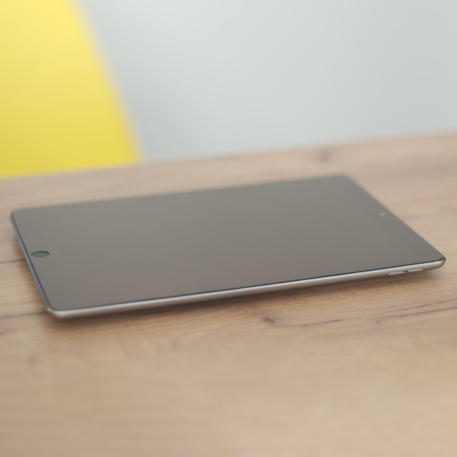 Ein silbernes Tablet liegt auf einem Holztisch und zeigt einen dunklen Bildschirm.