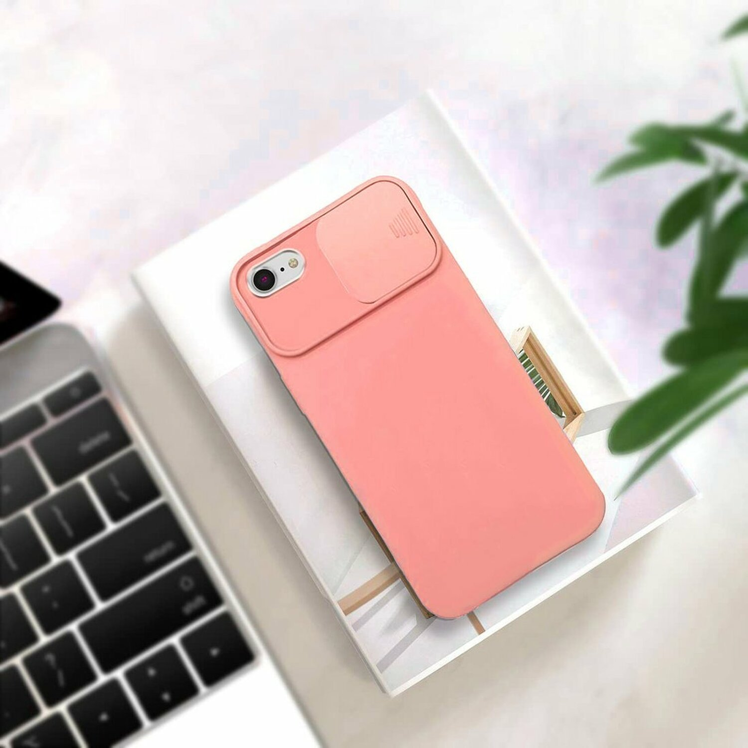Custodia per telefono rosa con copertura scorrevole per fotocamera, appoggiata su libri e un laptop.