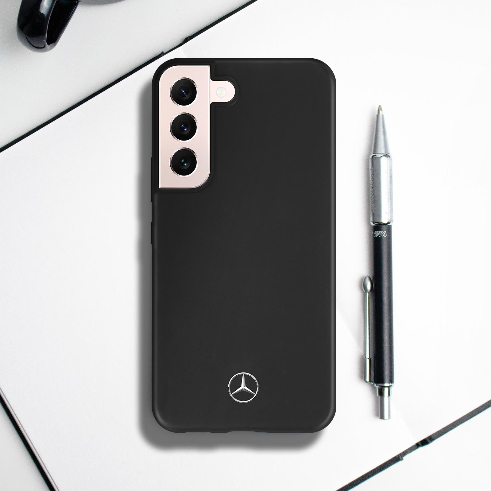 Schwarze Handyhülle mit Mercedes-Logo, ein Stift an der Seite. Der Hintergrund ist eine weiße Oberfläche.