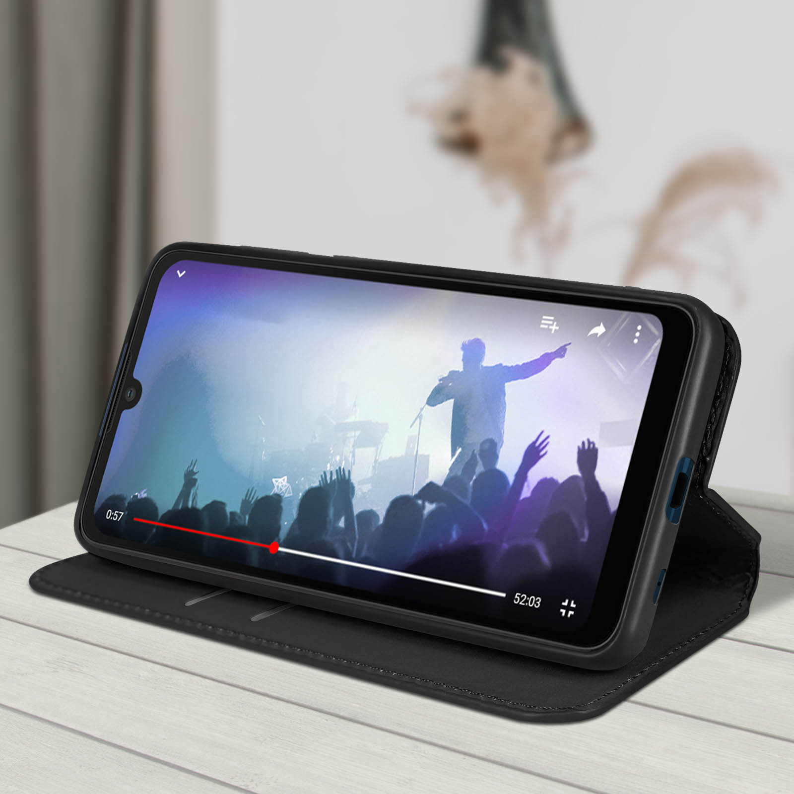 Telefono in custodia nera, che riproduce un video di un concerto su un tavolo.