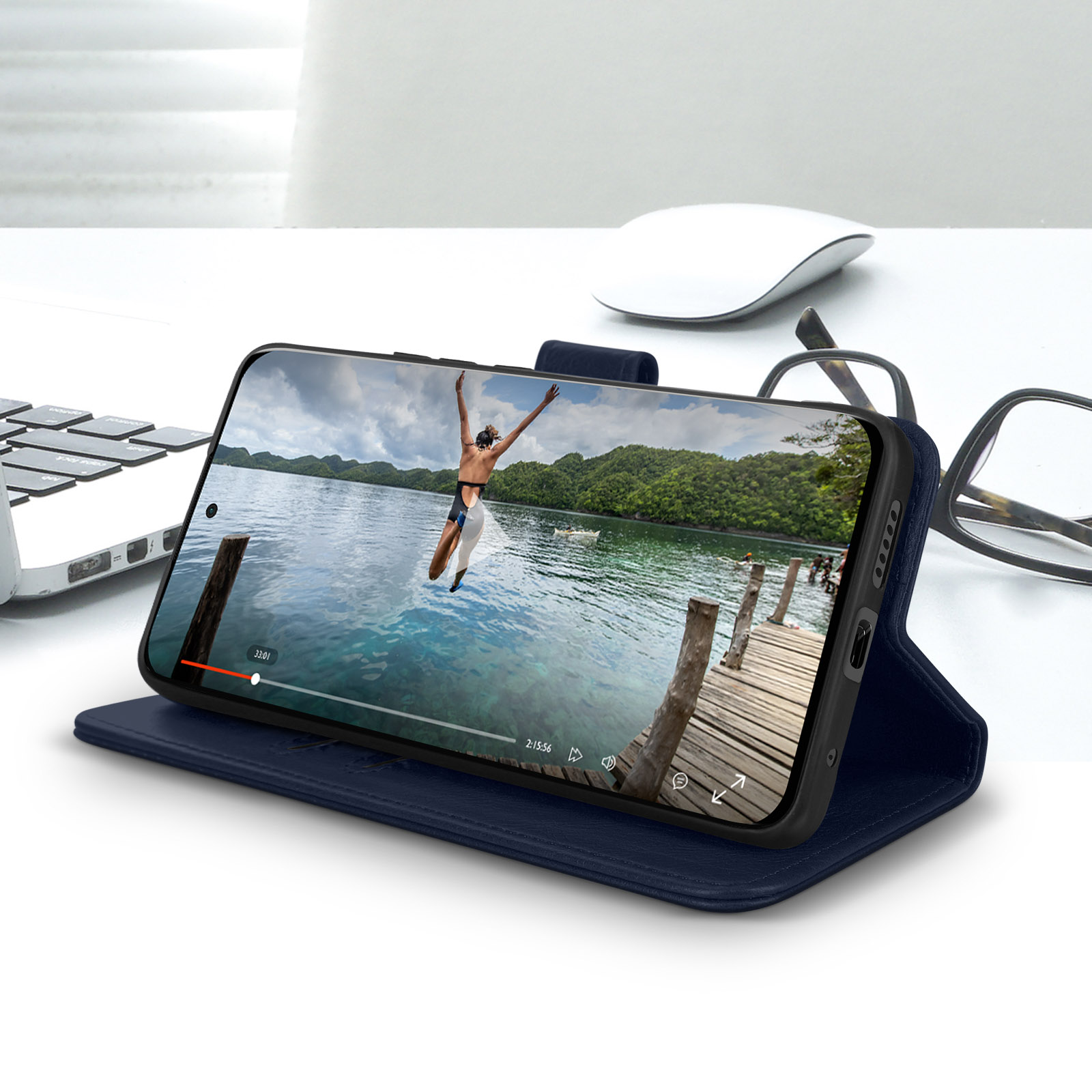 Un telefono in una custodia blu mostra un video di qualcuno che salta in acqua. Ci sono occhiali e un mouse nelle vicinanze.