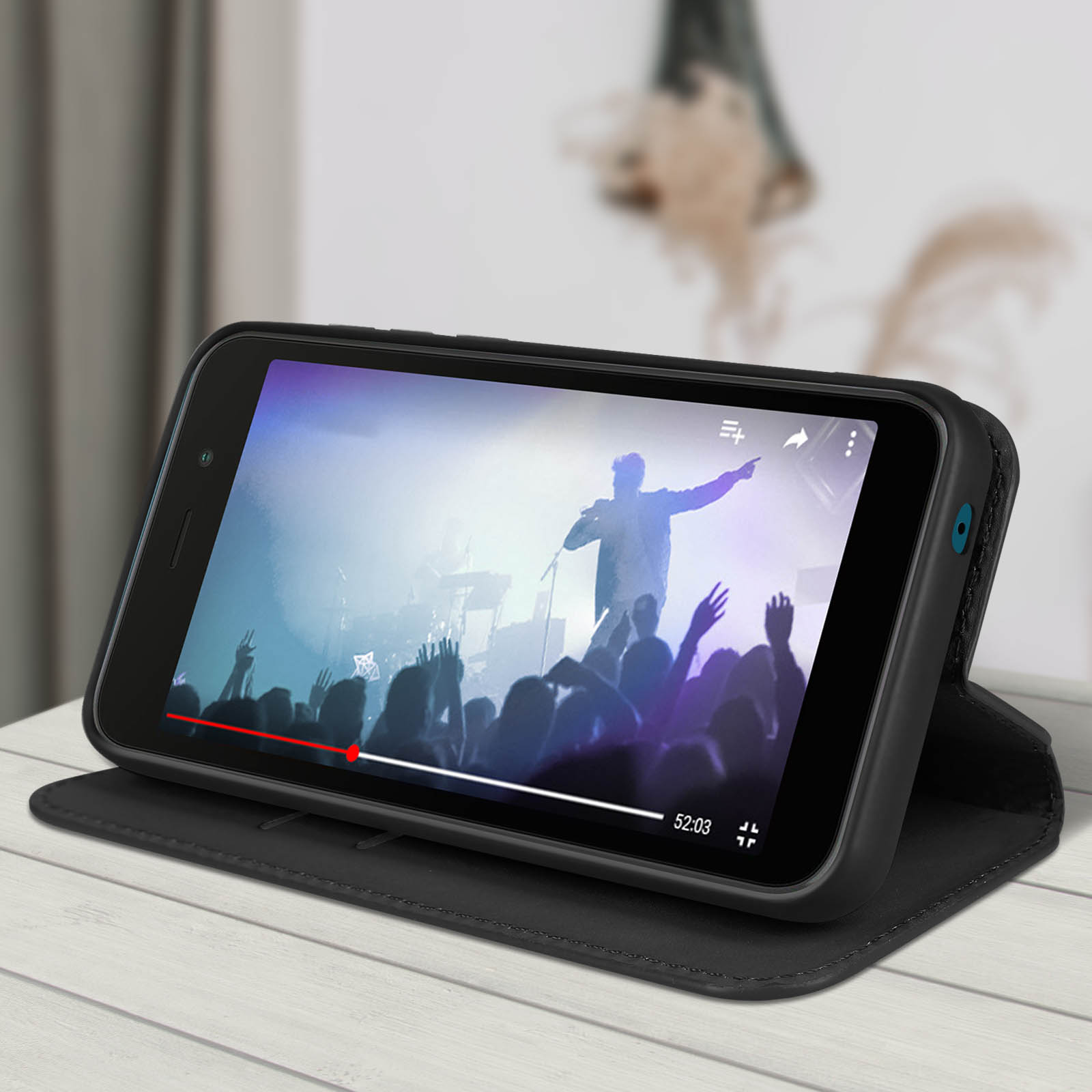 Een telefoon in een zwarte hoes toont een video van een concert. De telefoon staat op een houten oppervlak.