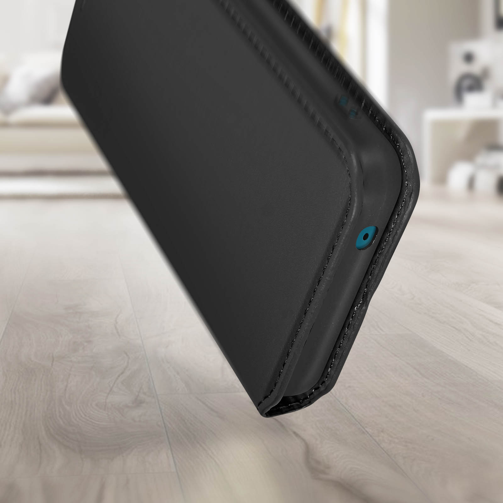 Close-up van een zwarte telefoonhoes. Op een houten vloer, zijkant met oplaadpoort zichtbaar.