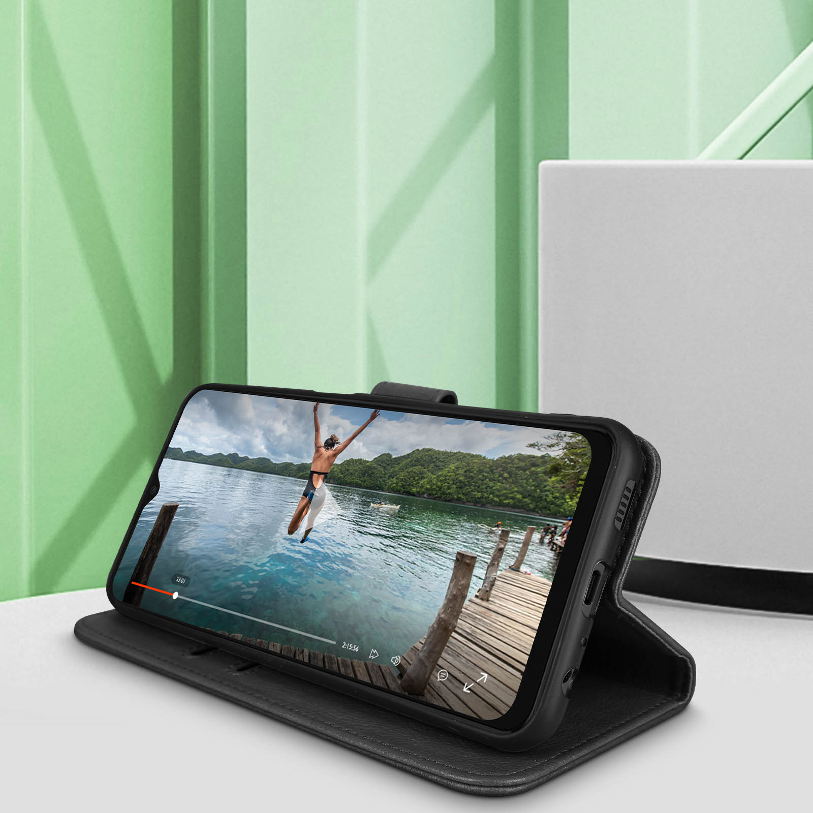 Zwarte telefoonhoes met telefoon die een video toont van een springende persoon, op een zwarte standaard.