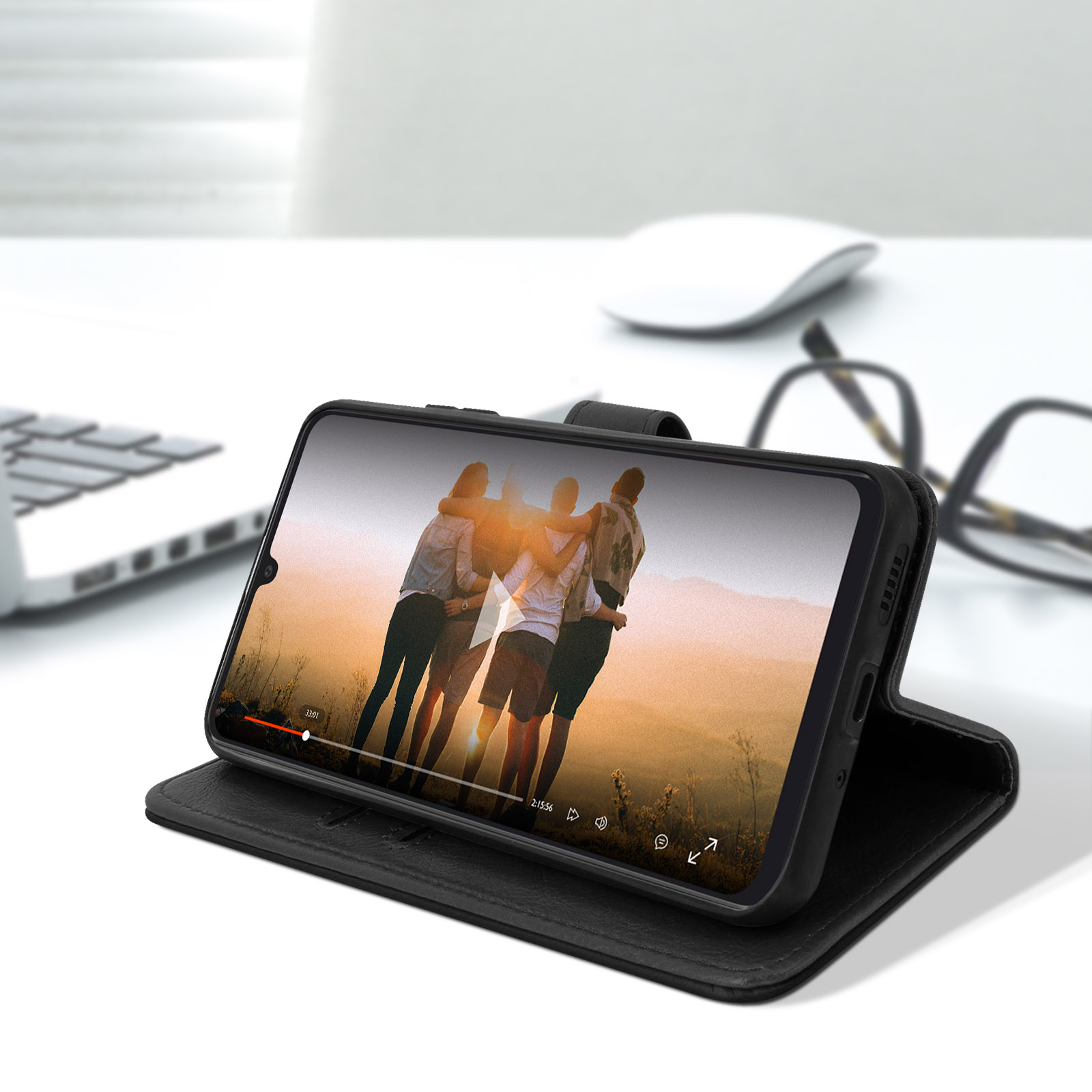 Un téléphone dans un étui en cuir noir lit une vidéo de personnes. Bureau blanc avec des lunettes et une souris.