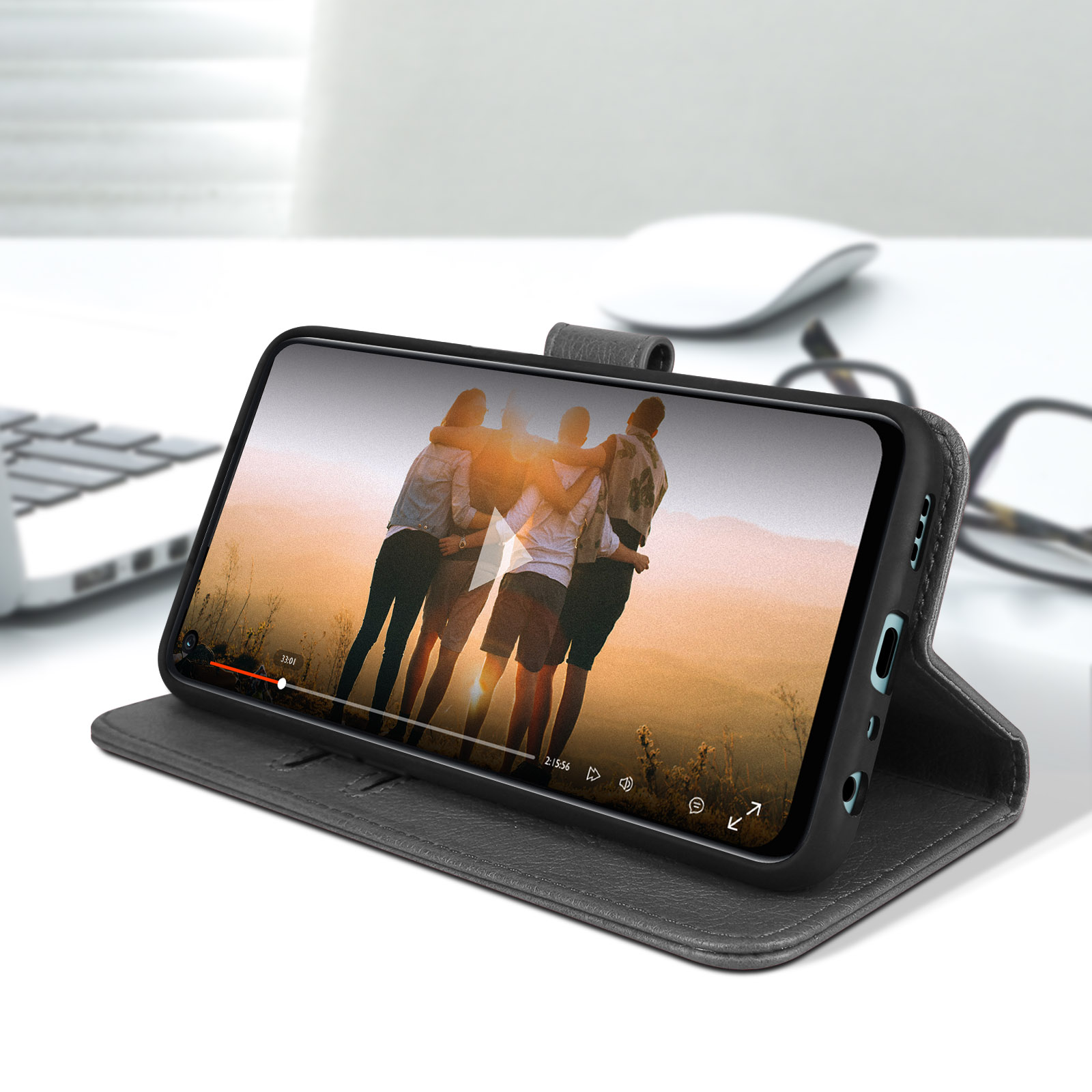 Uno smartphone mostra un video. È in una custodia grigia su una scrivania bianca, con un computer sullo sfondo.