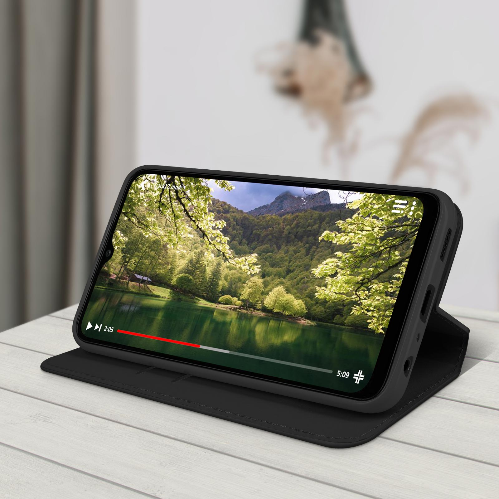 Ein Telefon zeigt ein Video eines Sees, umgeben von Bäumen, auf einem Holztisch.