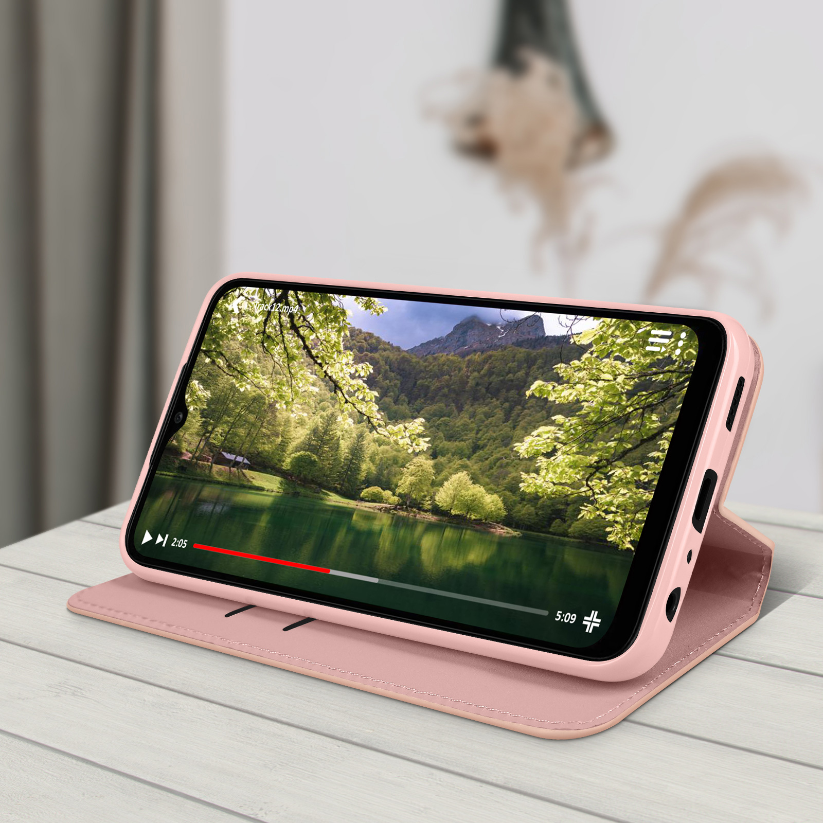 Un telefono in una custodia rosa che riproduce un video di un lago e alberi, su una superficie di legno.