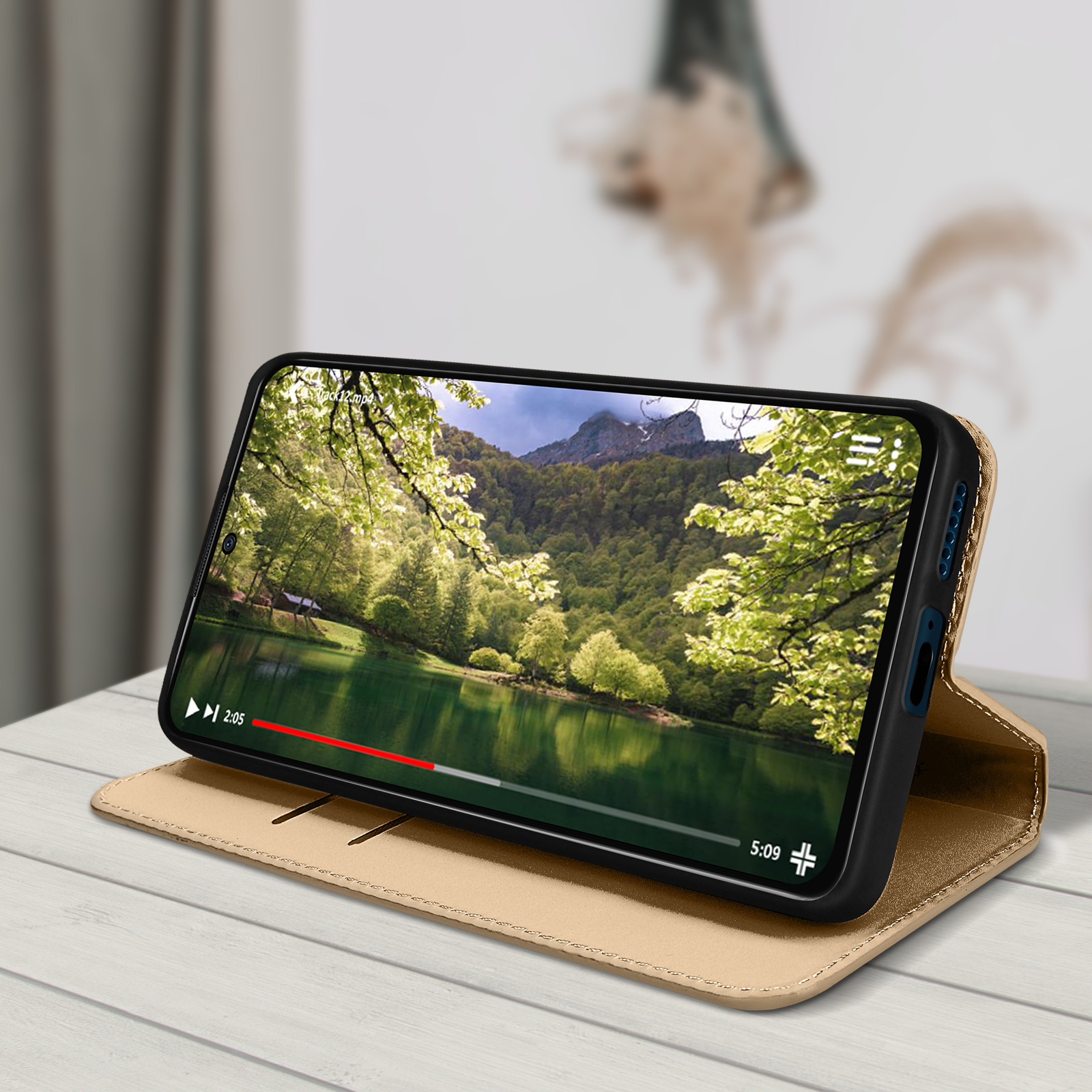 Un telefono che mostra un video su un tavolo di legno con una custodia dorata.