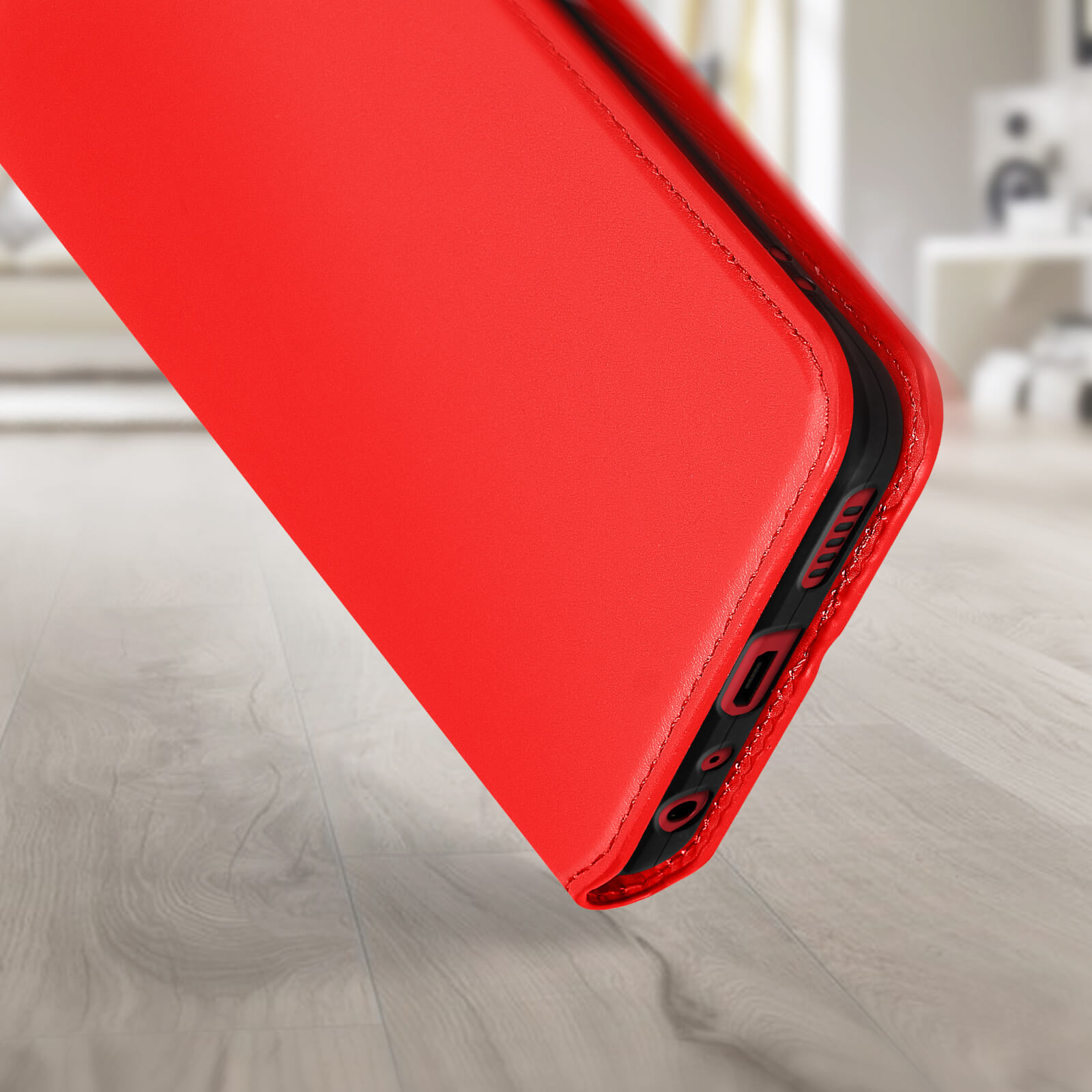 Custodia per telefono rossa, primo piano. È appoggiata su una superficie di legno. Lo sfondo è sfocato.