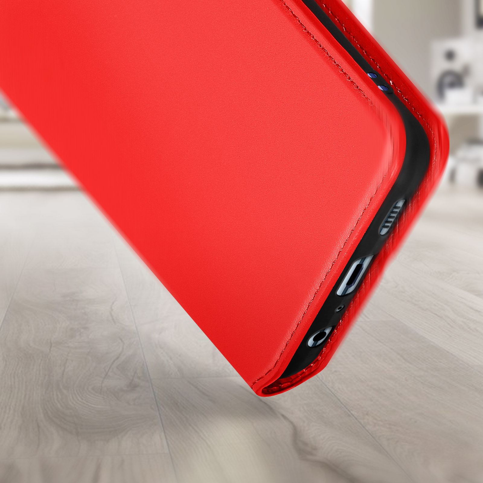 Een rode telefoonhoes is schuin geplaatst en toont de zijkant met poorten. Een houten vloer is op de voorgrond.