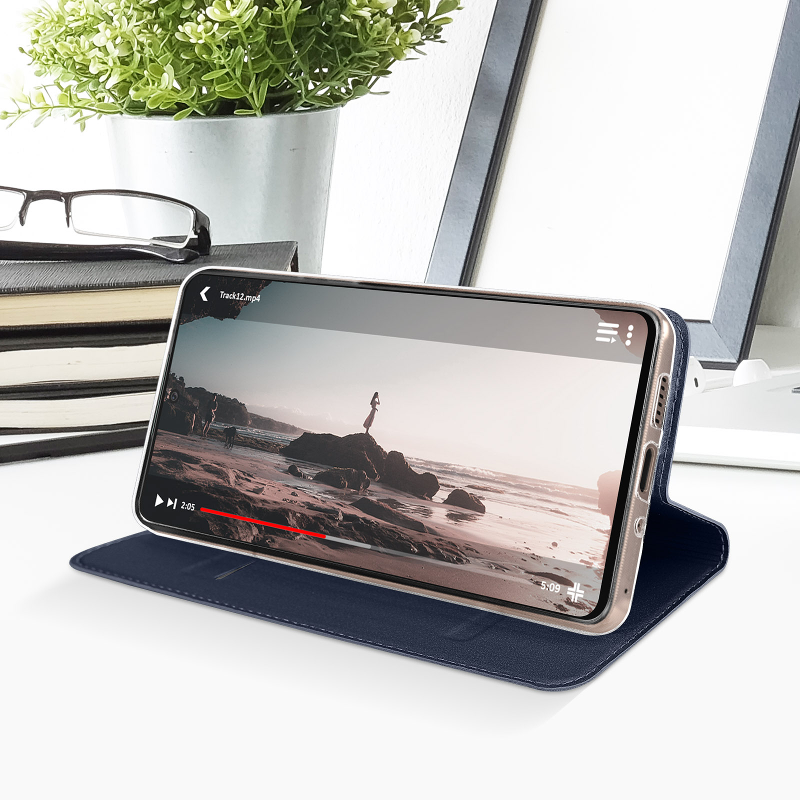Un telefono in una custodia blu è su un tavolo. Lo schermo mostra un video sulla spiaggia.