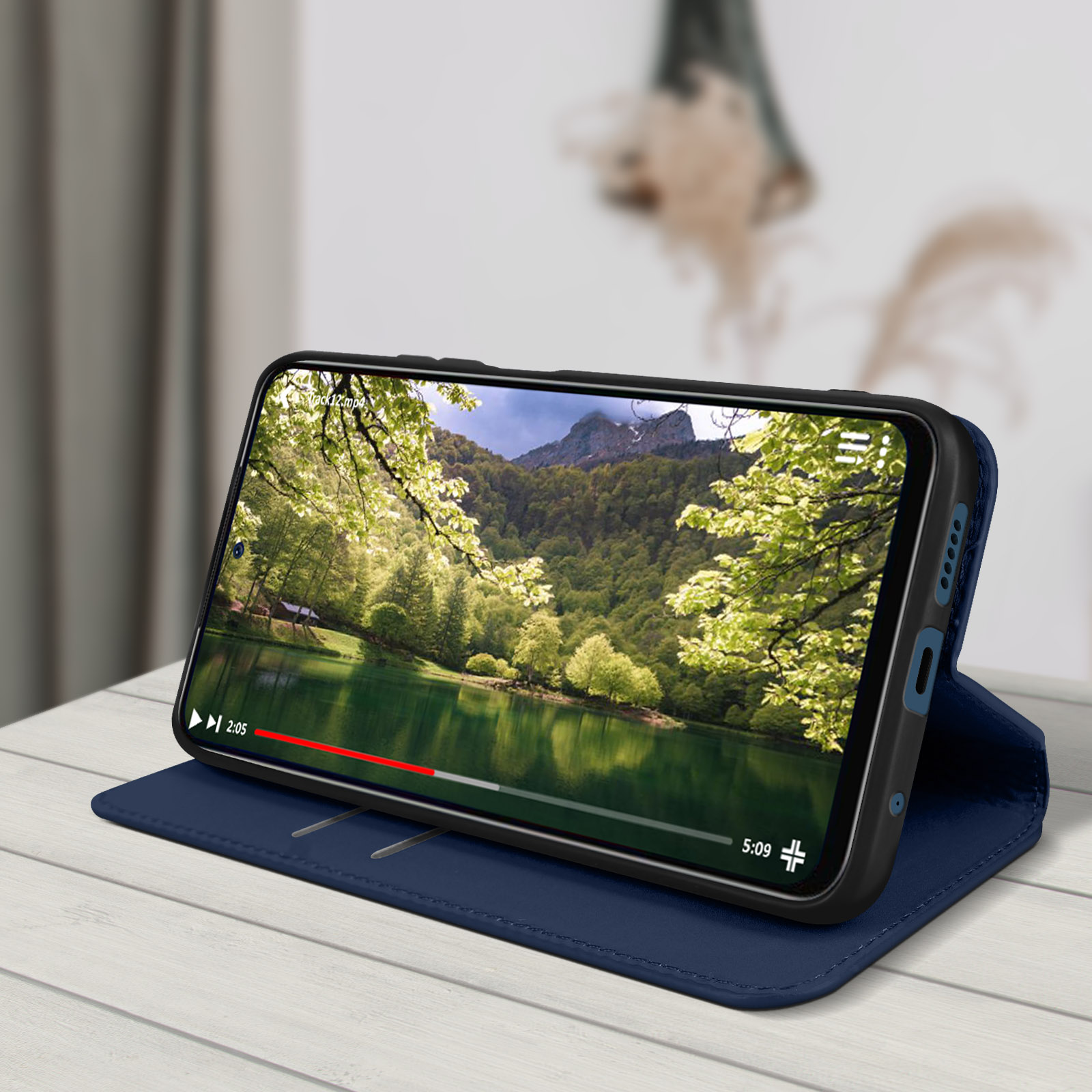 Téléphone dans un étui bleu, affichant une vidéo d'un lac et d'arbres verts.