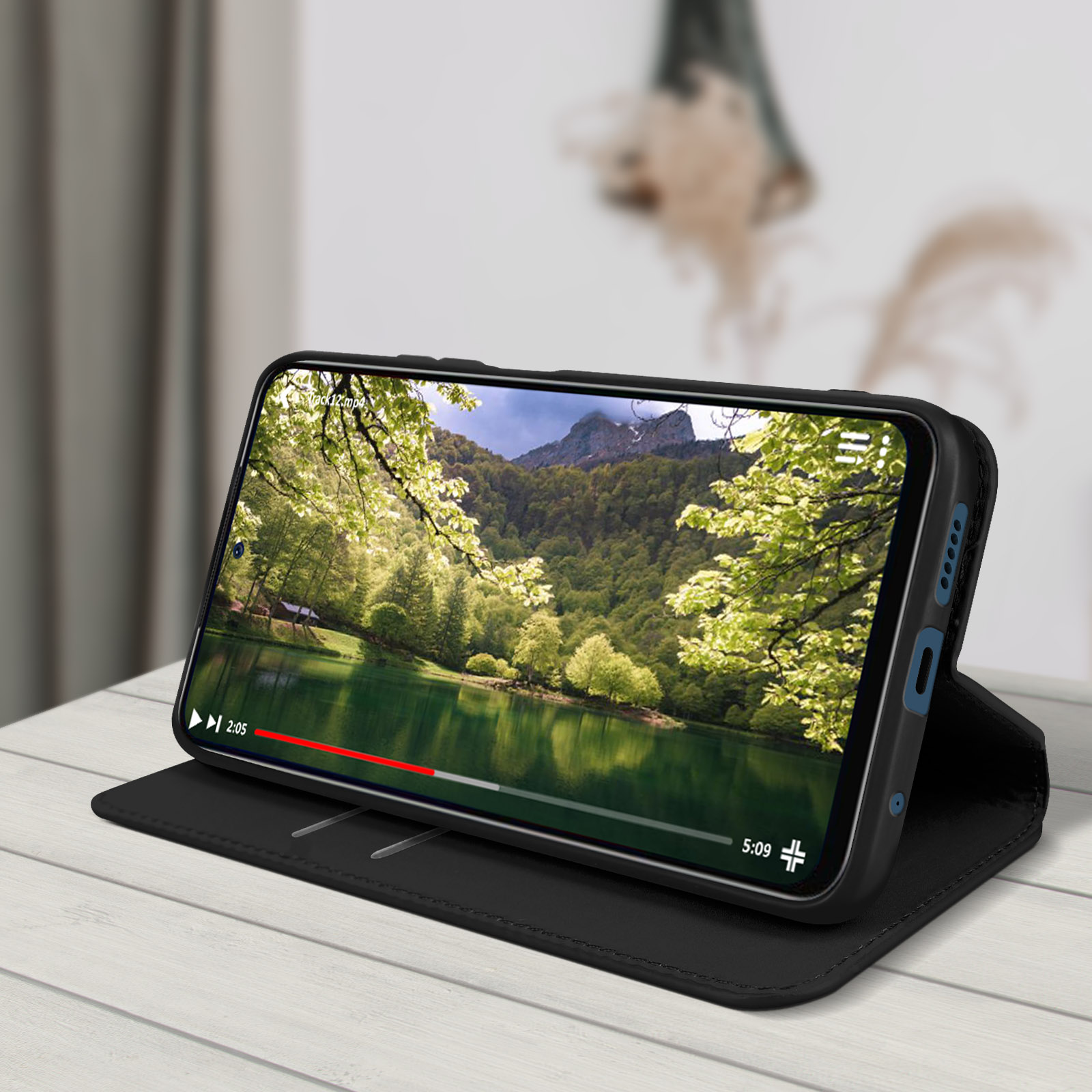 Téléphone noir dans un étui noir. Le téléphone affiche une vidéo d'un lac et d'une forêt.