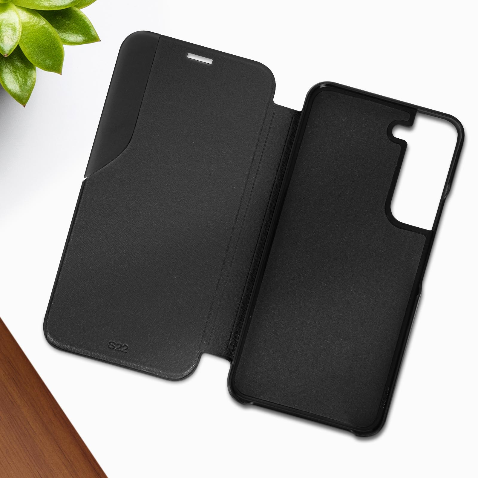 Geöffnete schwarze Handyhülle mit Telefon darin, auf weißer Oberfläche. Grüne Pflanze in Ecke.