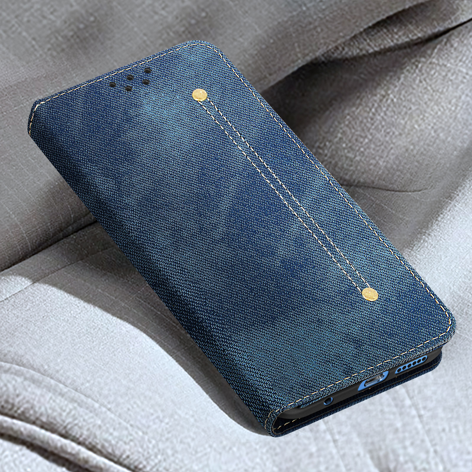 Custodia per telefono in denim blu, chiusa, con cuciture bianche. La custodia è su una superficie in tessuto grigio.