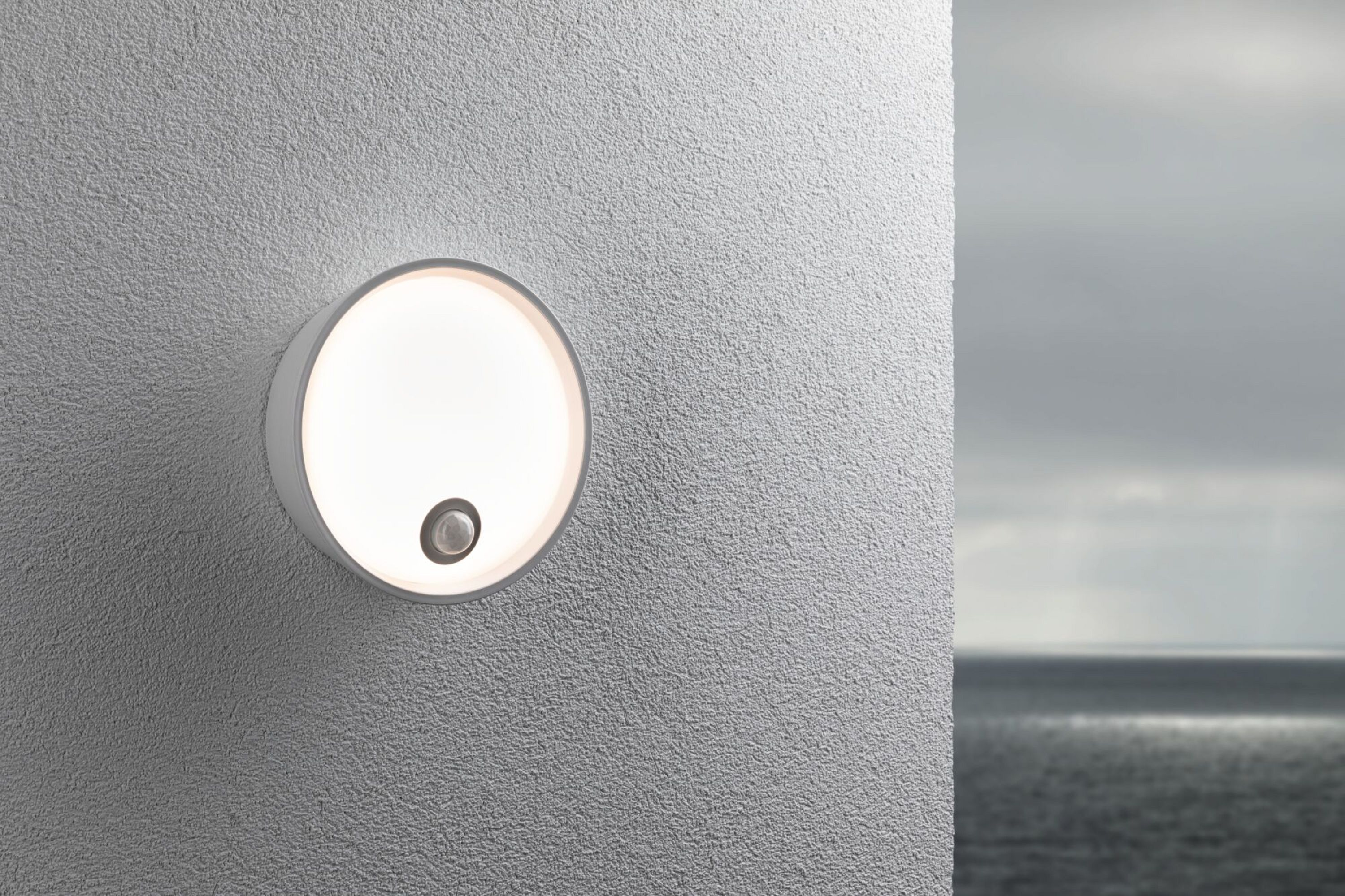 Runde weiße Wandlampe, die Licht ausstrahlt, an einer strukturierten Wand montiert.