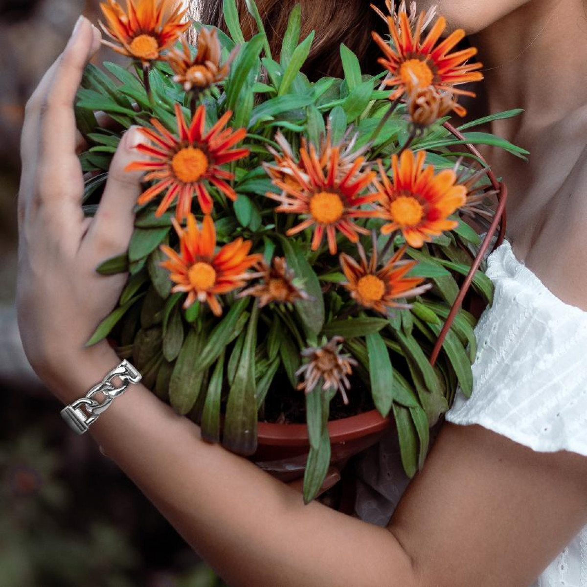 Una persona che tiene un vaso di fiori arancioni con un braccialetto al polso.