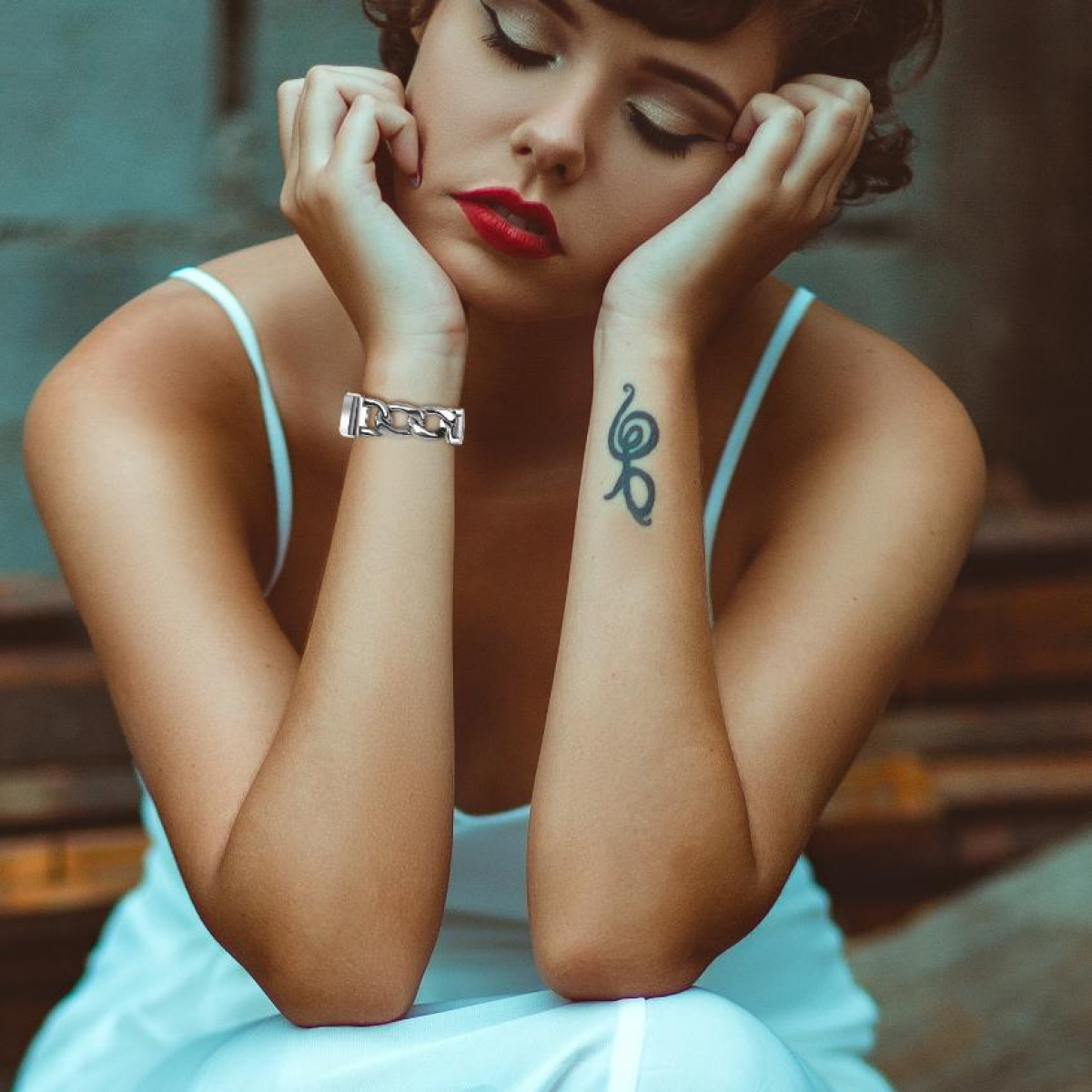Donna con rossetto rosso che si tiene il viso. Tatuaggio sul polso. Abito bianco.