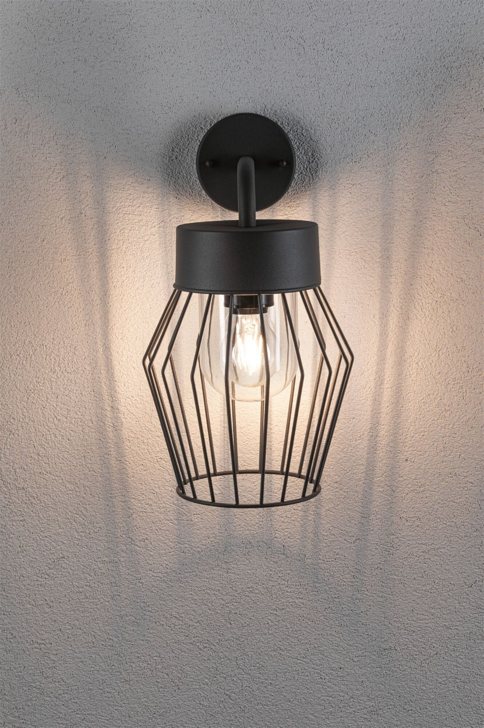 Eine schwarze Wandlampe mit käfigartigem Lampenschirm, an einer grauen Wand.