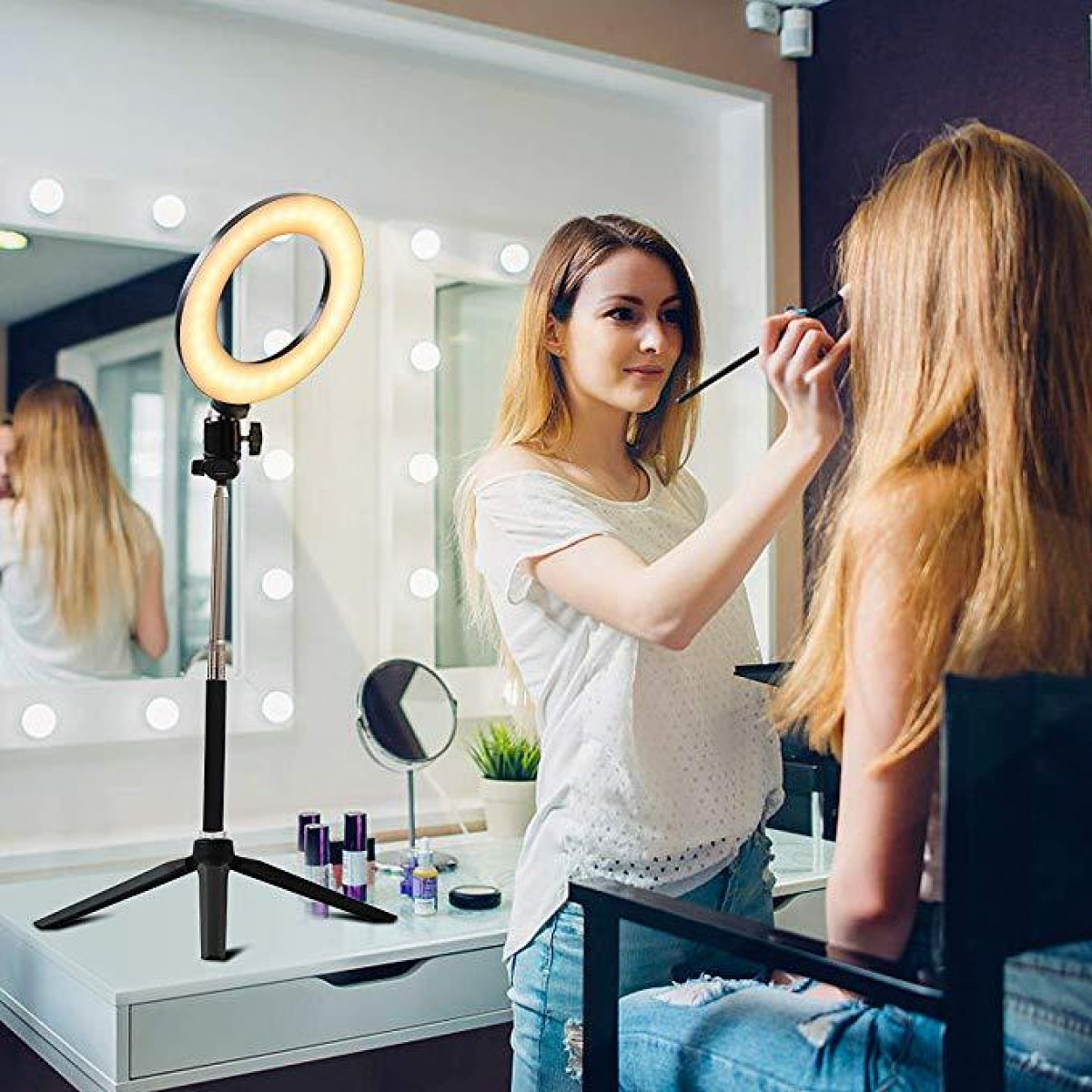 Eine Frau, die einer anderen Frau unter einem Ringlicht in einem Make-up-Studio Make-up aufträgt.
