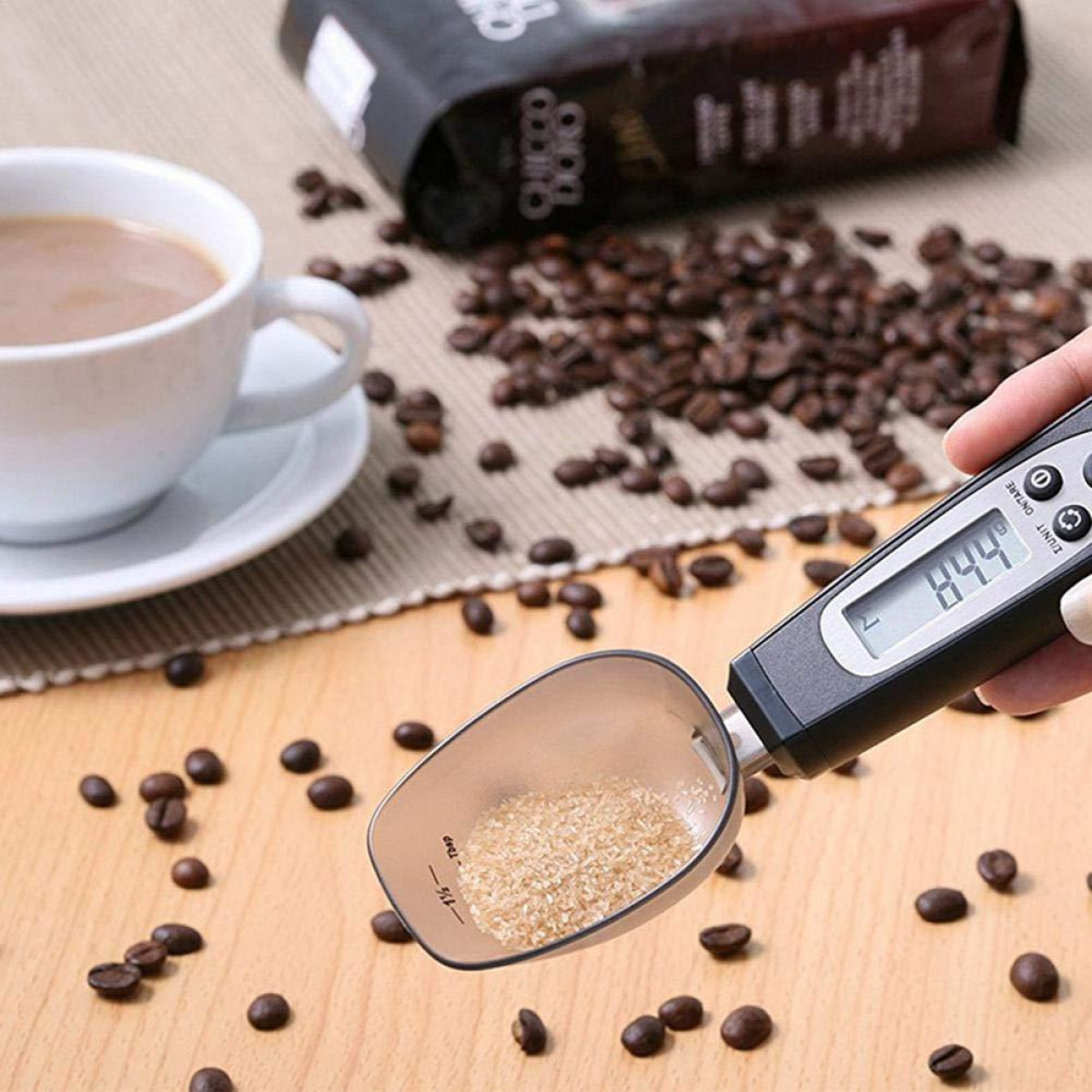 Łyżka z cukrem i ziarnami kawy. Ręka trzyma łyżkę z wagą cyfrową.