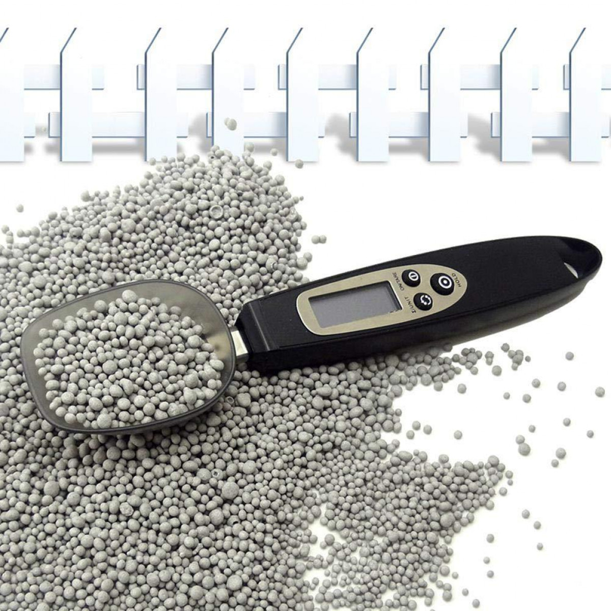 Łyżka z szarymi granulkami nawozu i wagą na białym tle.