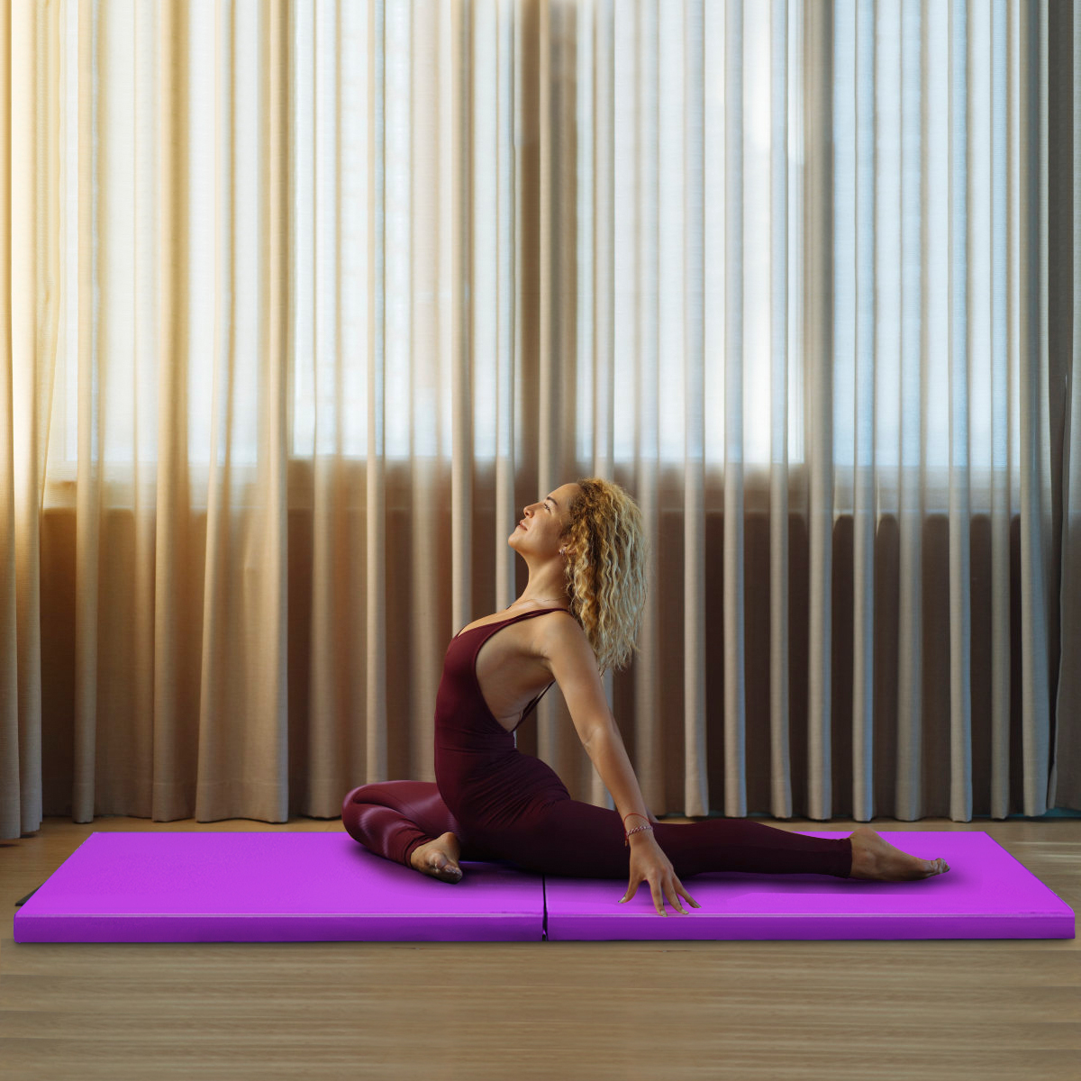 Eine Frau in einem weinroten Outfit macht Yoga auf einer lila Matte in der Nähe eines Fensters.