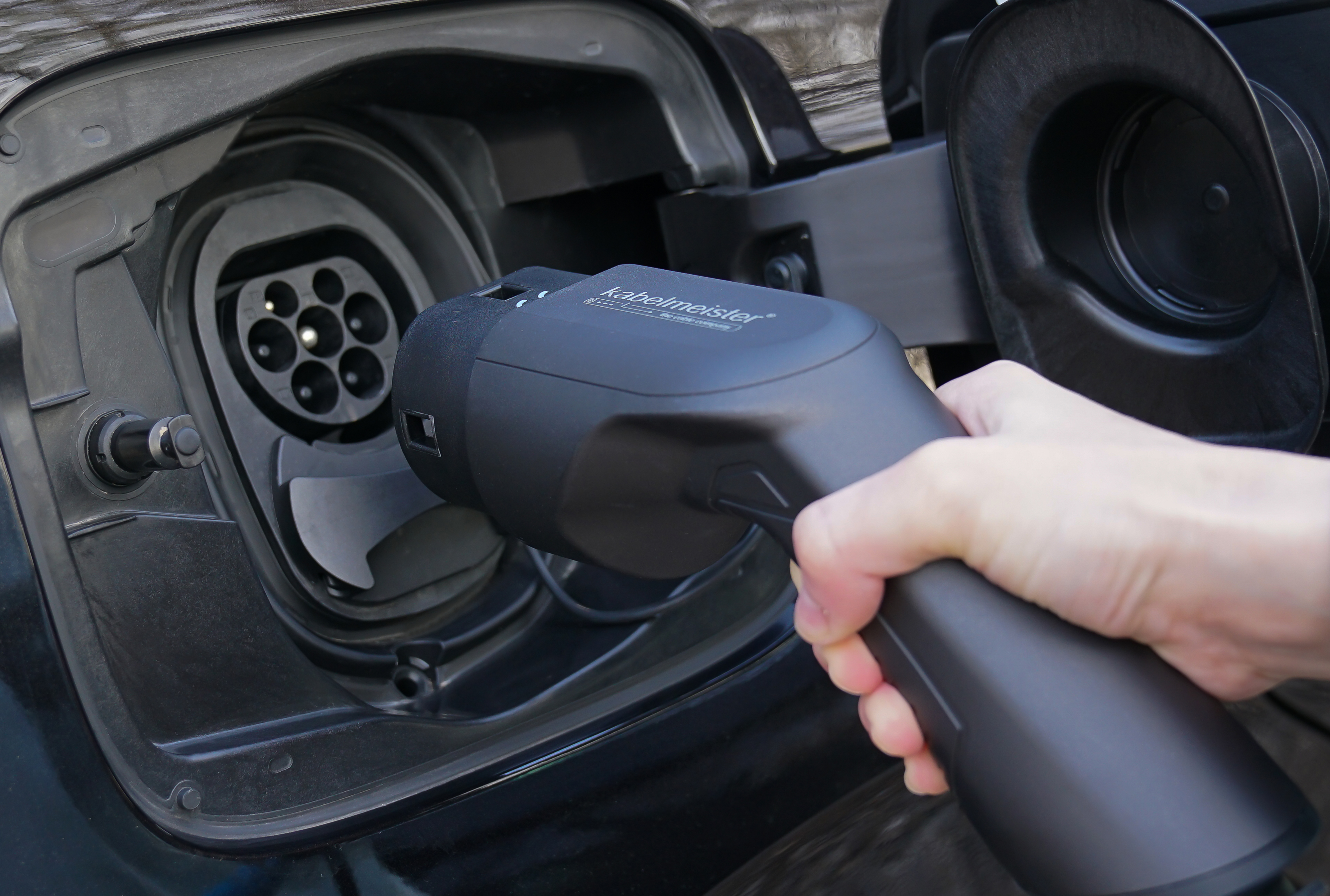 Hand steckt Ladegerät in den Ladeanschluss eines Elektrofahrzeugs.