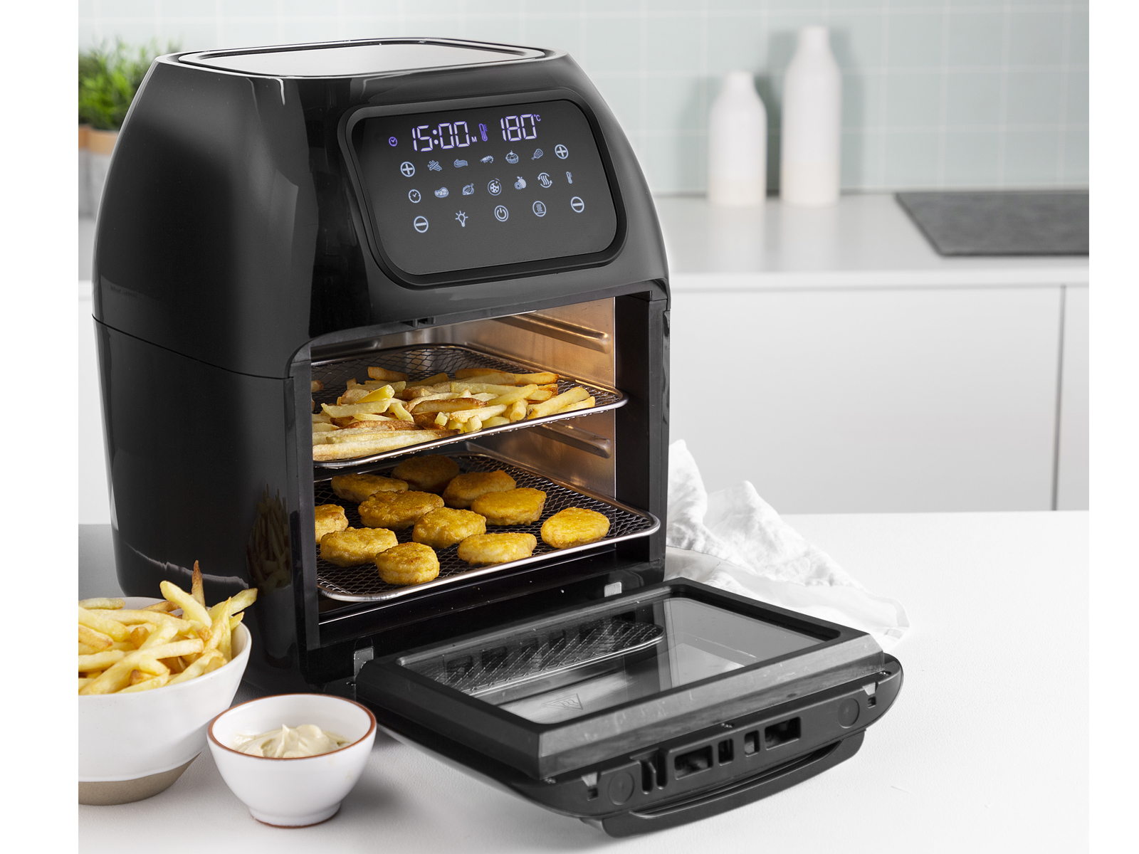 Czarna frytkownica powietrzna z jedzeniem w koszach. Posiada wyświetlacz cyfrowy i elementy sterujące.
