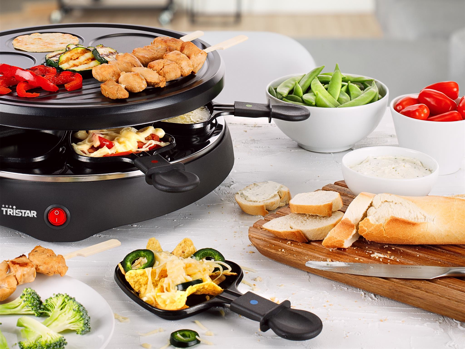 Ein Raclette-Grill mit Essen oben und Zutaten in der Nähe.