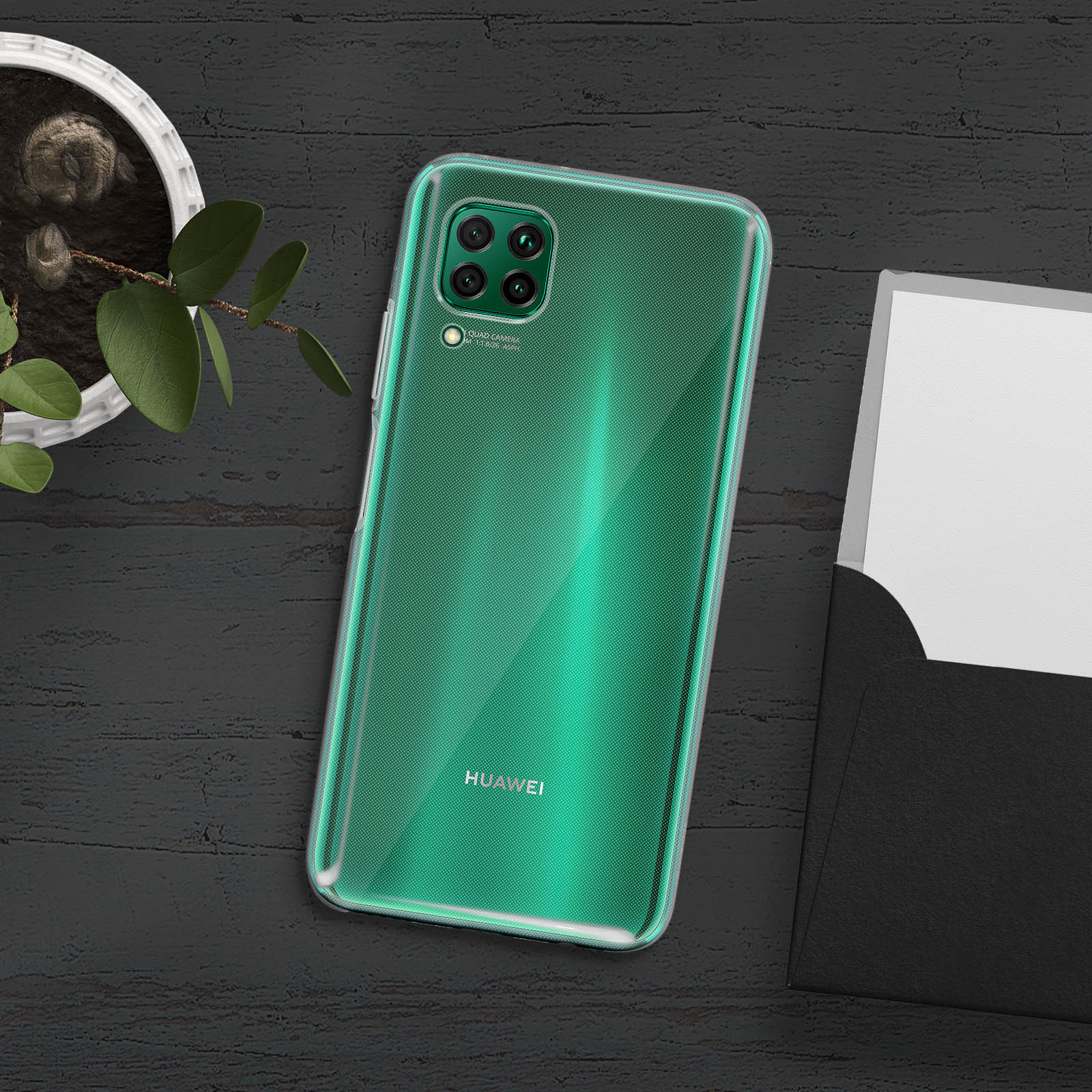 Zielony telefon w przezroczystym etui na czarnym stole z rośliną i papierem. Widoczne logo Huawei.