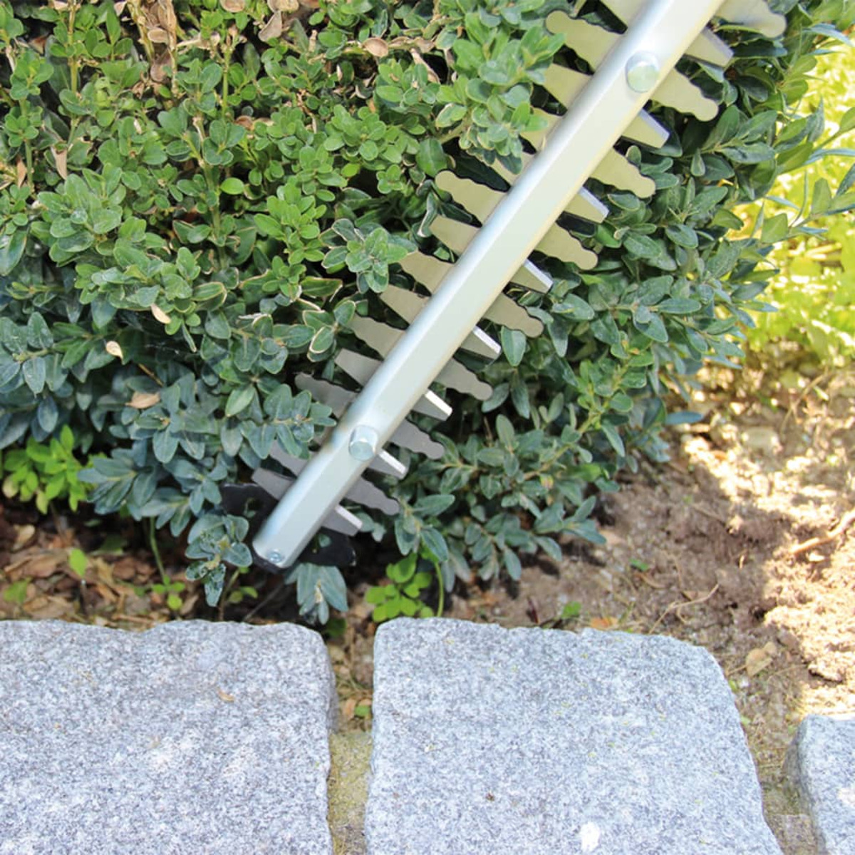 Nożyce do żywopłotu z ostrzami tnącymi zielony krzew w pobliżu szarych kamieni brukowych.