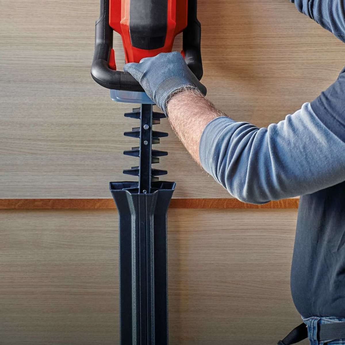 Personne tenant un taille-haie devant un mur en bois.