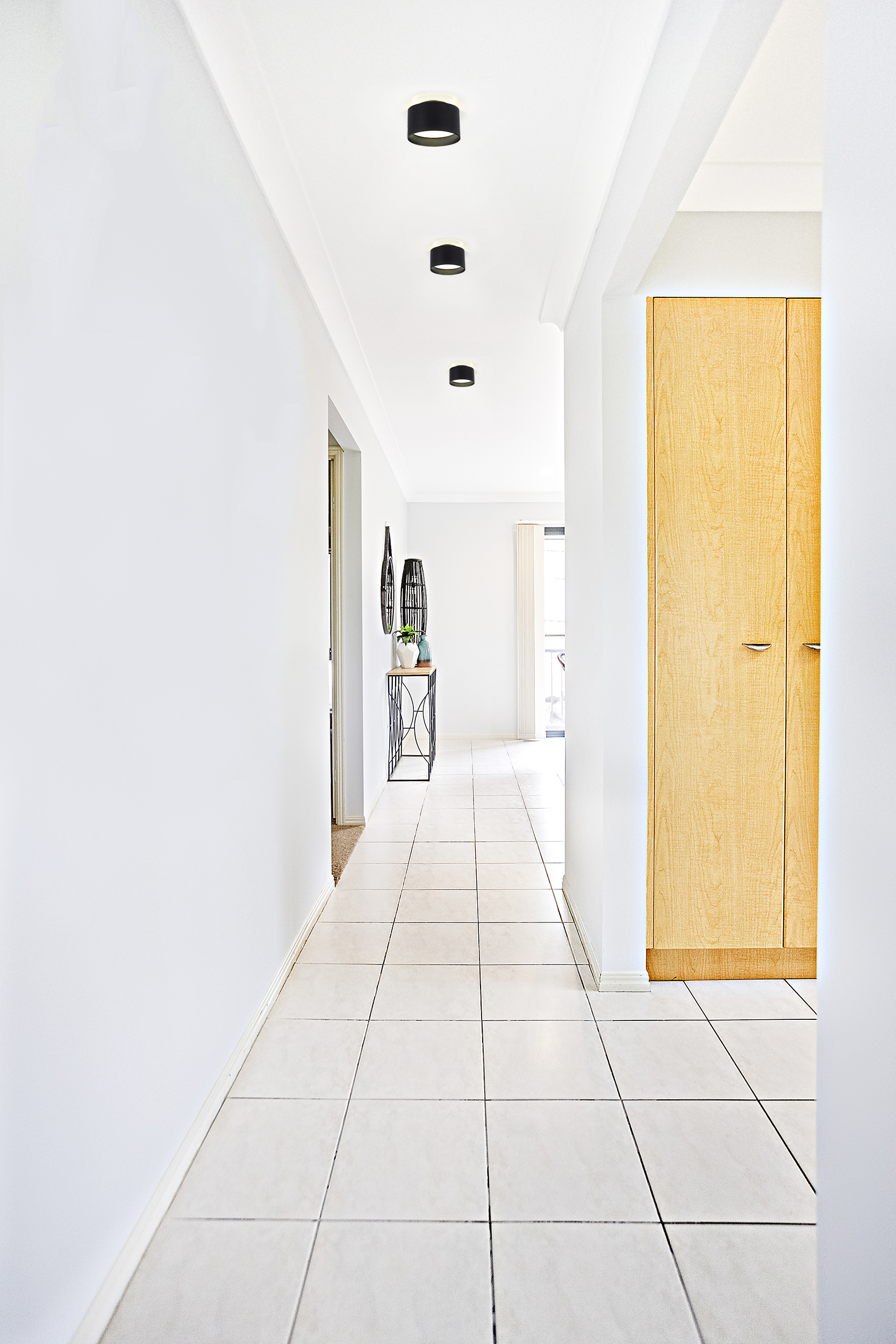 Flur mit weißen Wänden, Fliesenboden, Einbaustrahlern und einem Holzschrank.