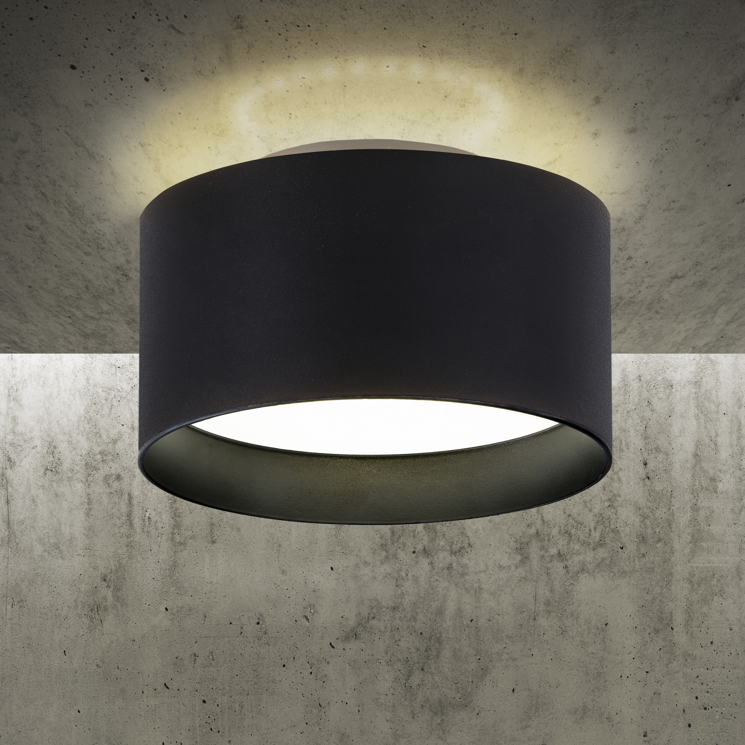 Eine schwarze zylindrische Lampe hängt von einer Betondecke. Das Licht scheint nach unten.