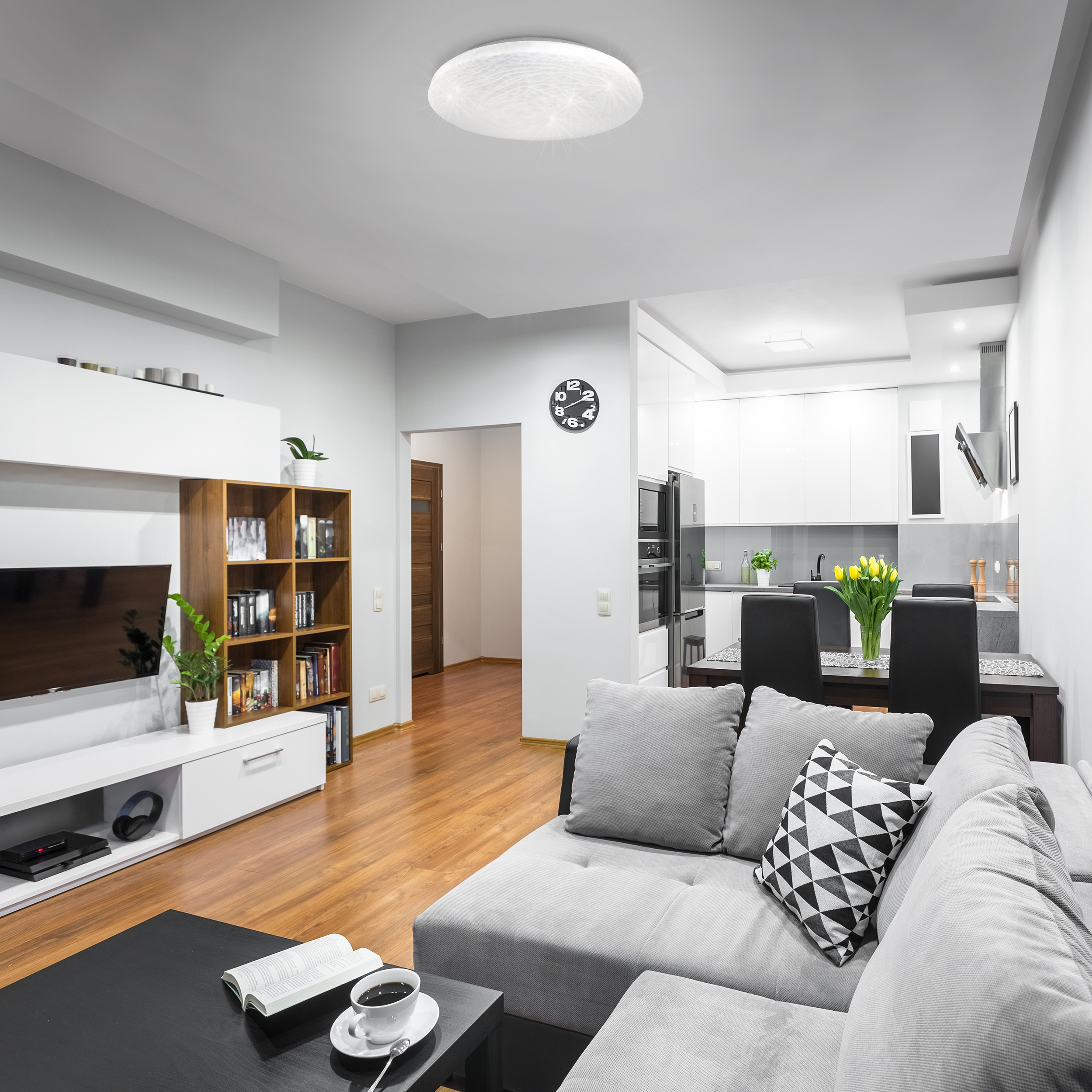 Ein modernes Wohnzimmer mit grauem Sofa, schwarzem Tisch und weißer Küche im Hintergrund.