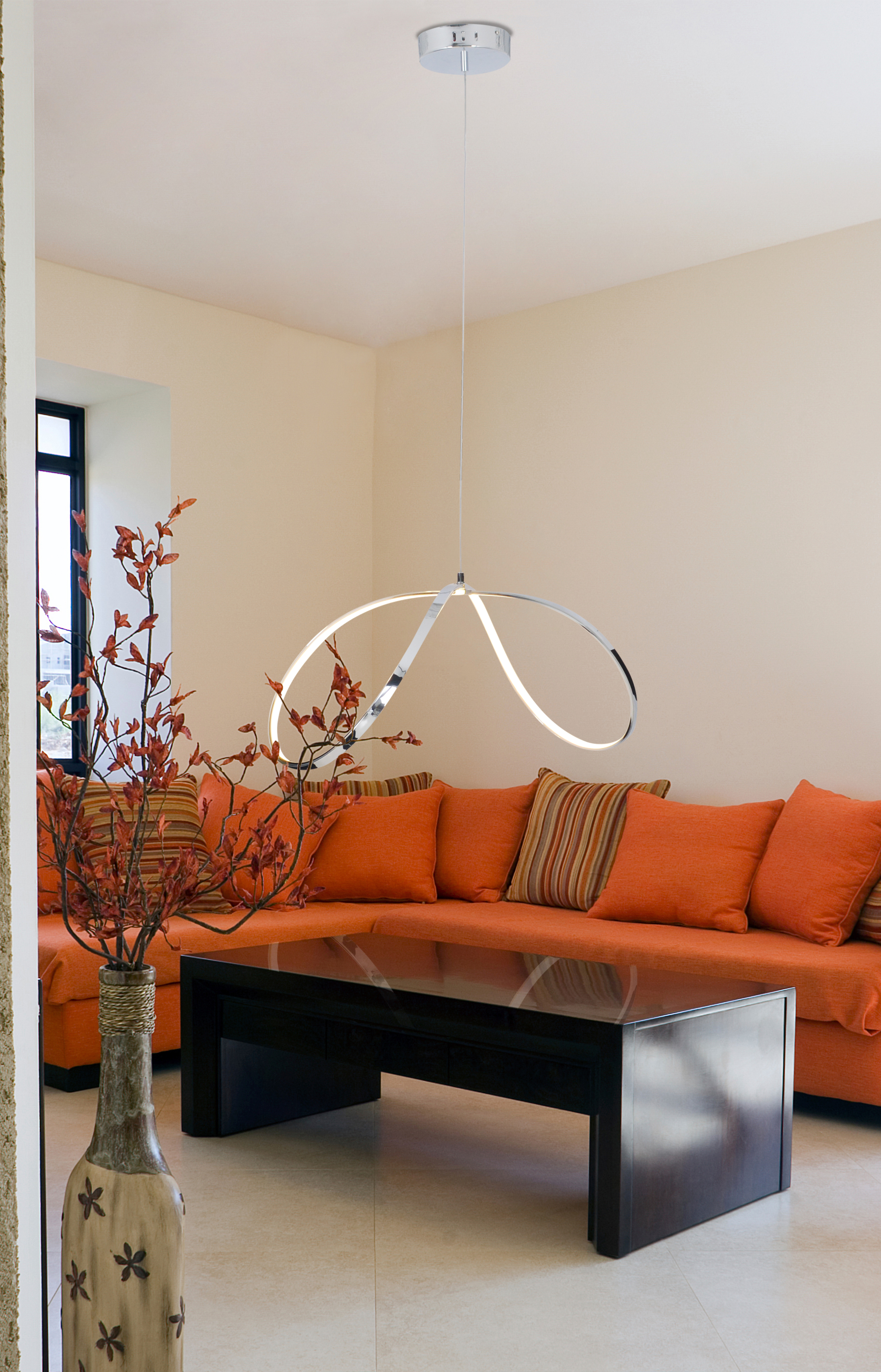Wohnzimmer mit orangefarbener Couch, schwarzem Couchtisch, Hängelampe und Vase mit Laub.