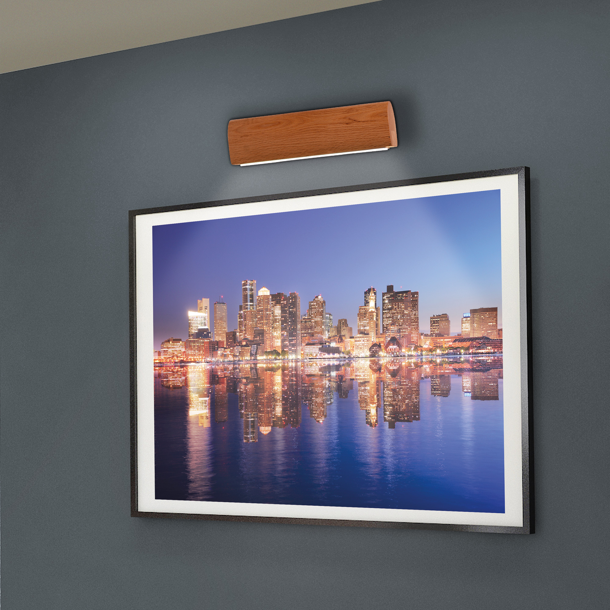 Ein gerahmtes Bild einer Skyline bei Nacht mit einer Holzleuchte darüber an einer Wand.