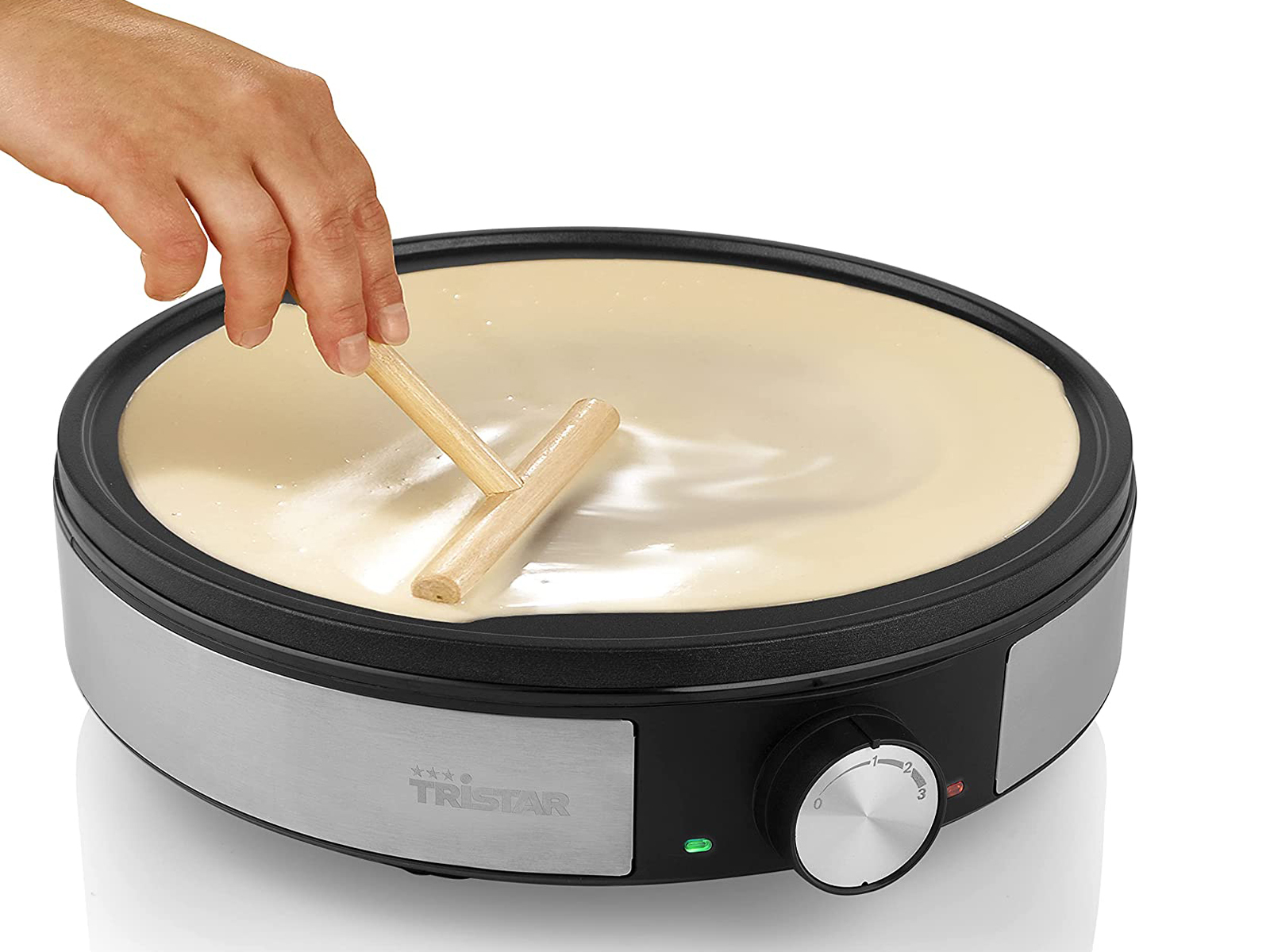 Osoba rozprowadza ciasto na naleśnikarce drewnianym narzędziem. Naleśnikarka jest czarna i srebrna.