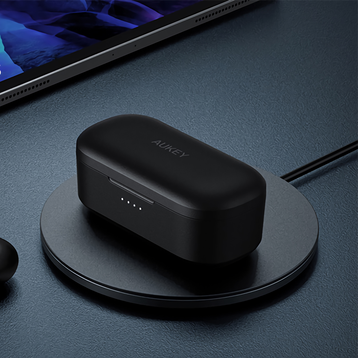 Auricolari wireless AUKEY neri in carica su un pad circolare nero.